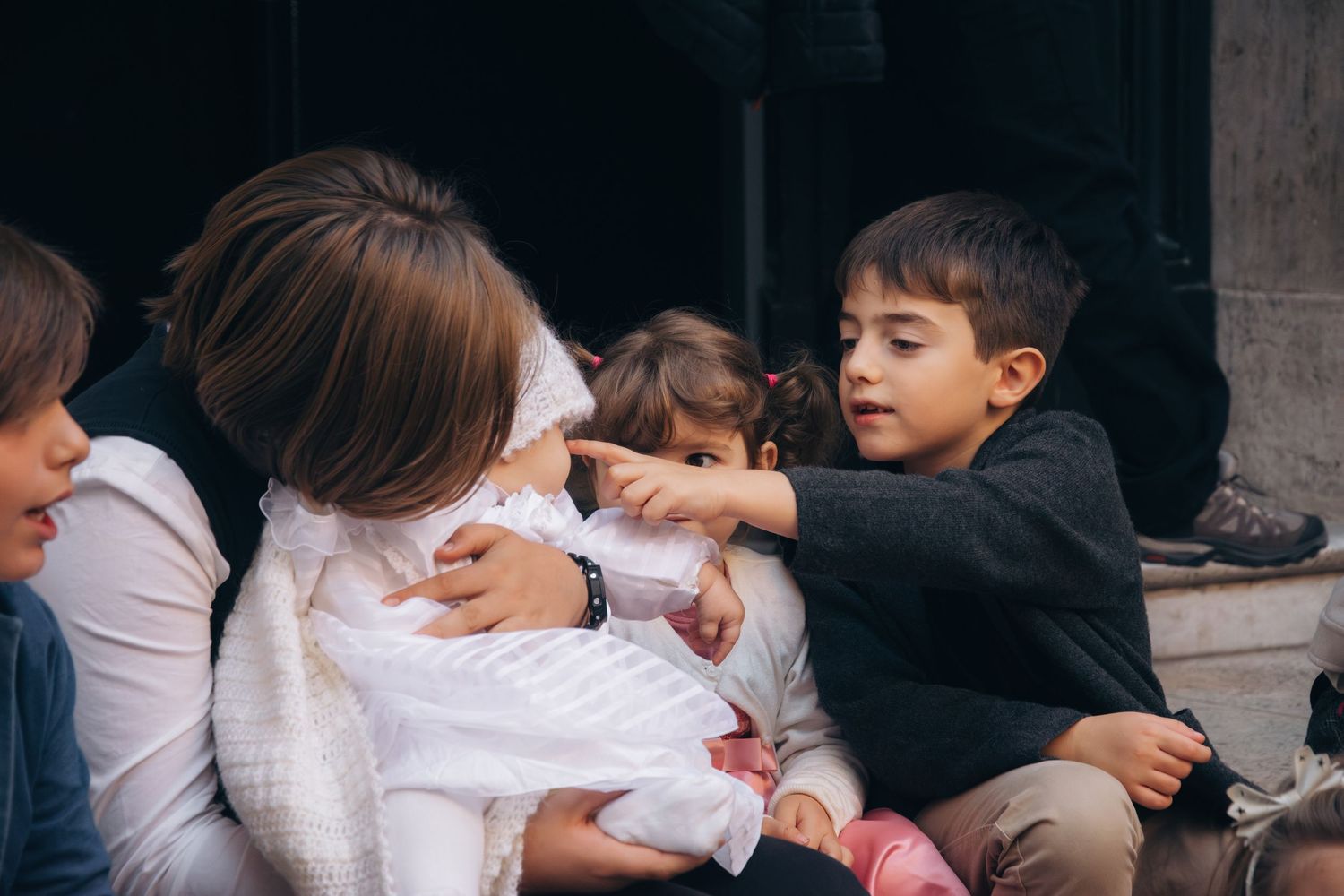 A group gathers around a baby dressed in white clothing indoors.