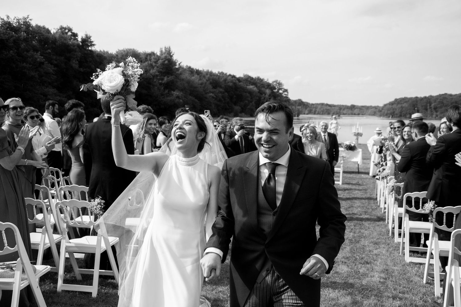 A joyful couple celebrates while walking down the aisle at their outdoor waterfront wedding ceremony.