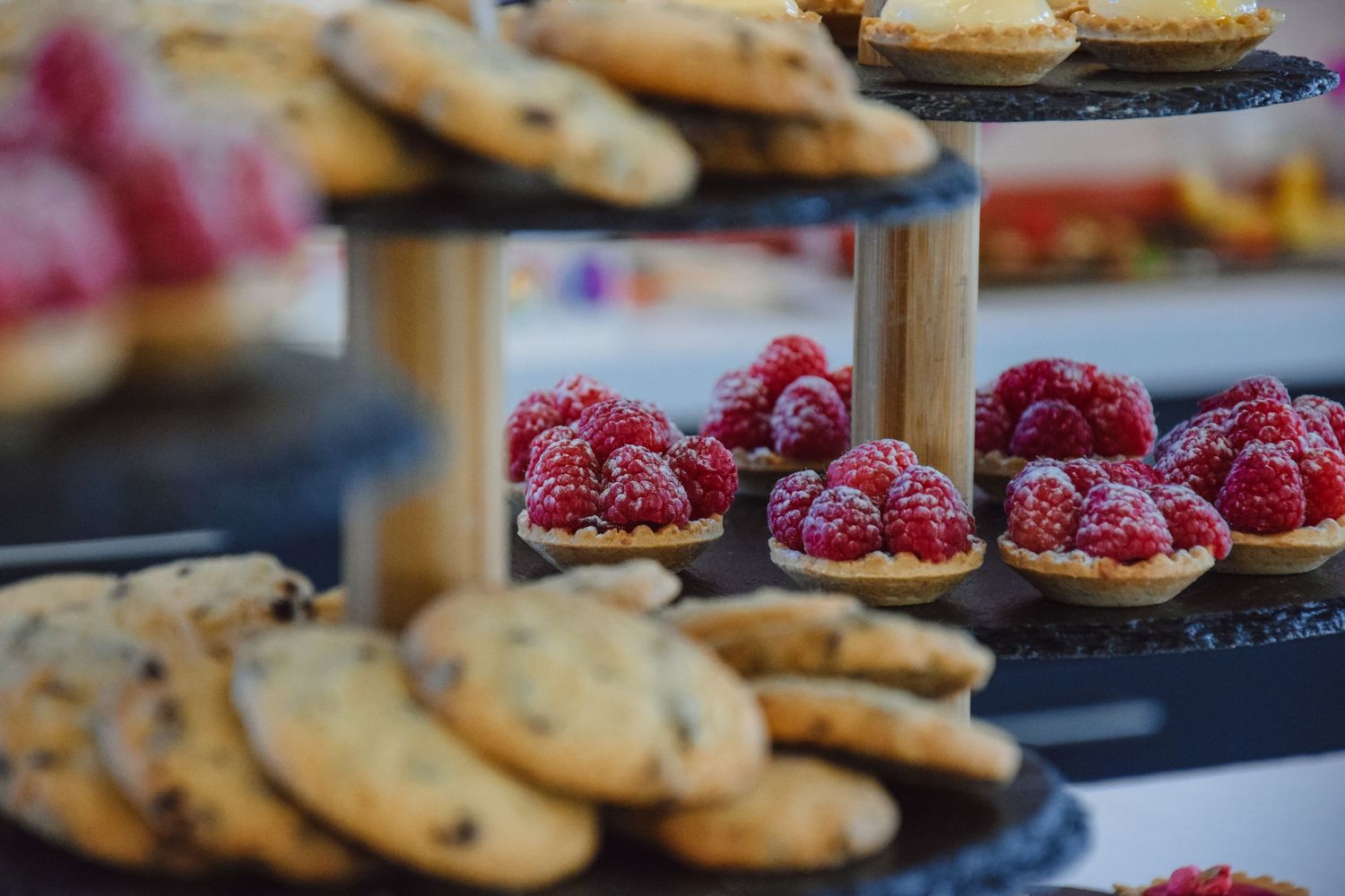 Fresh raspberry tarts and chocolate chip cookies displayed on tiered serving platters.