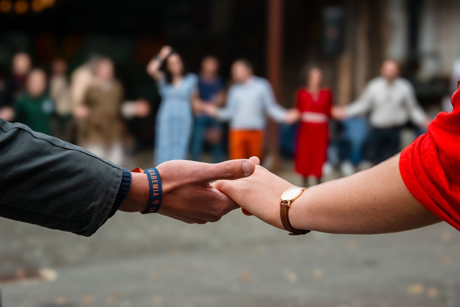 Two hands joining together in a gentle grasp with people dancing in a blurred background.