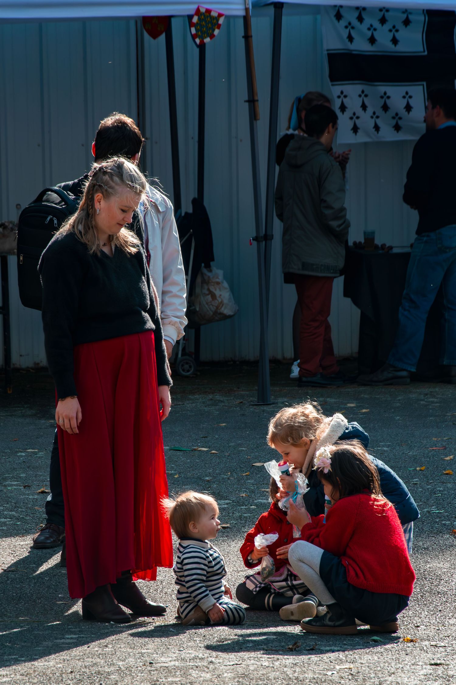 A group gathers outdoors on a sunny day wearing red and black clothing while interacting on the ground.