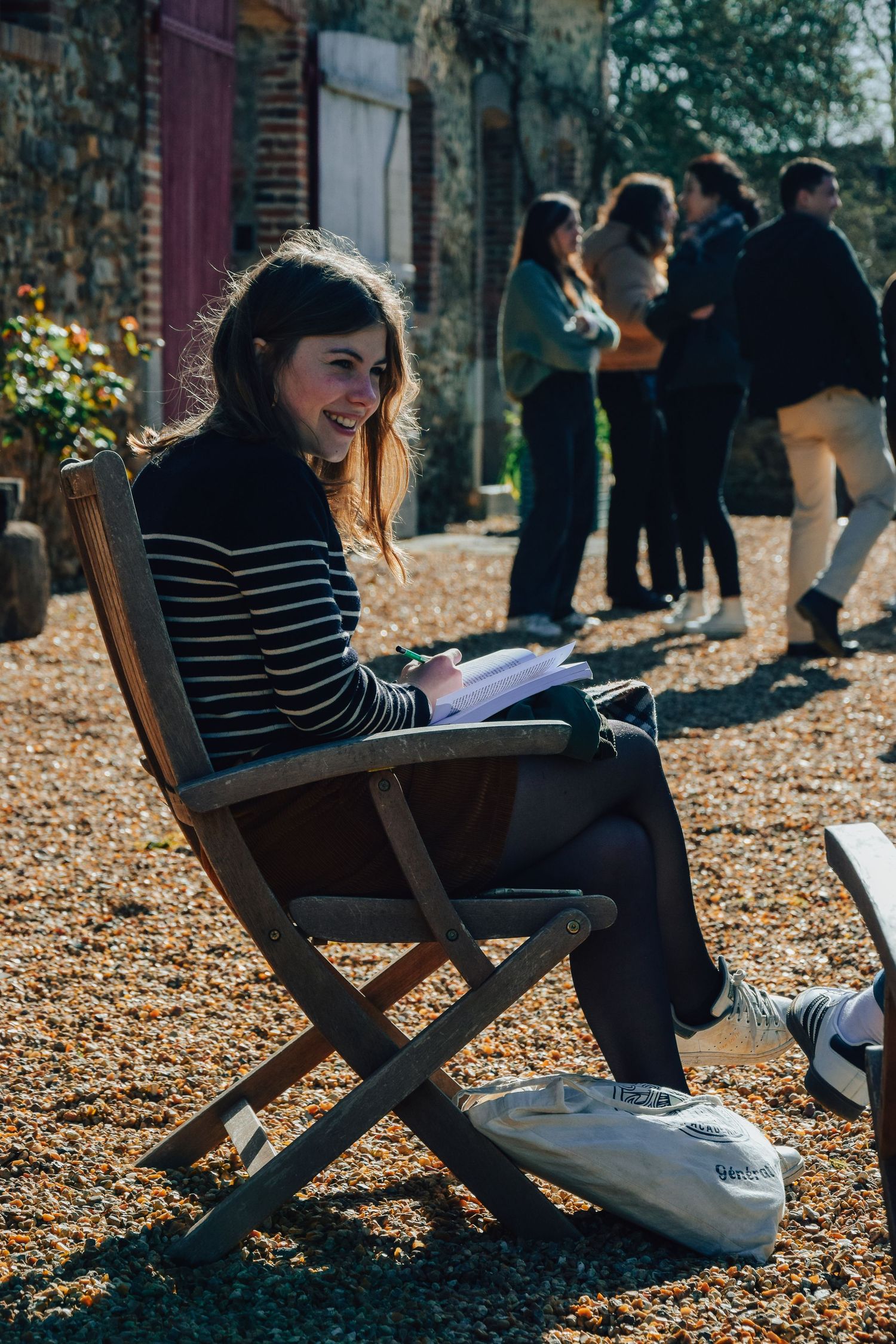 Person in striped sweater sitting in folding chair outdoors with others in background.