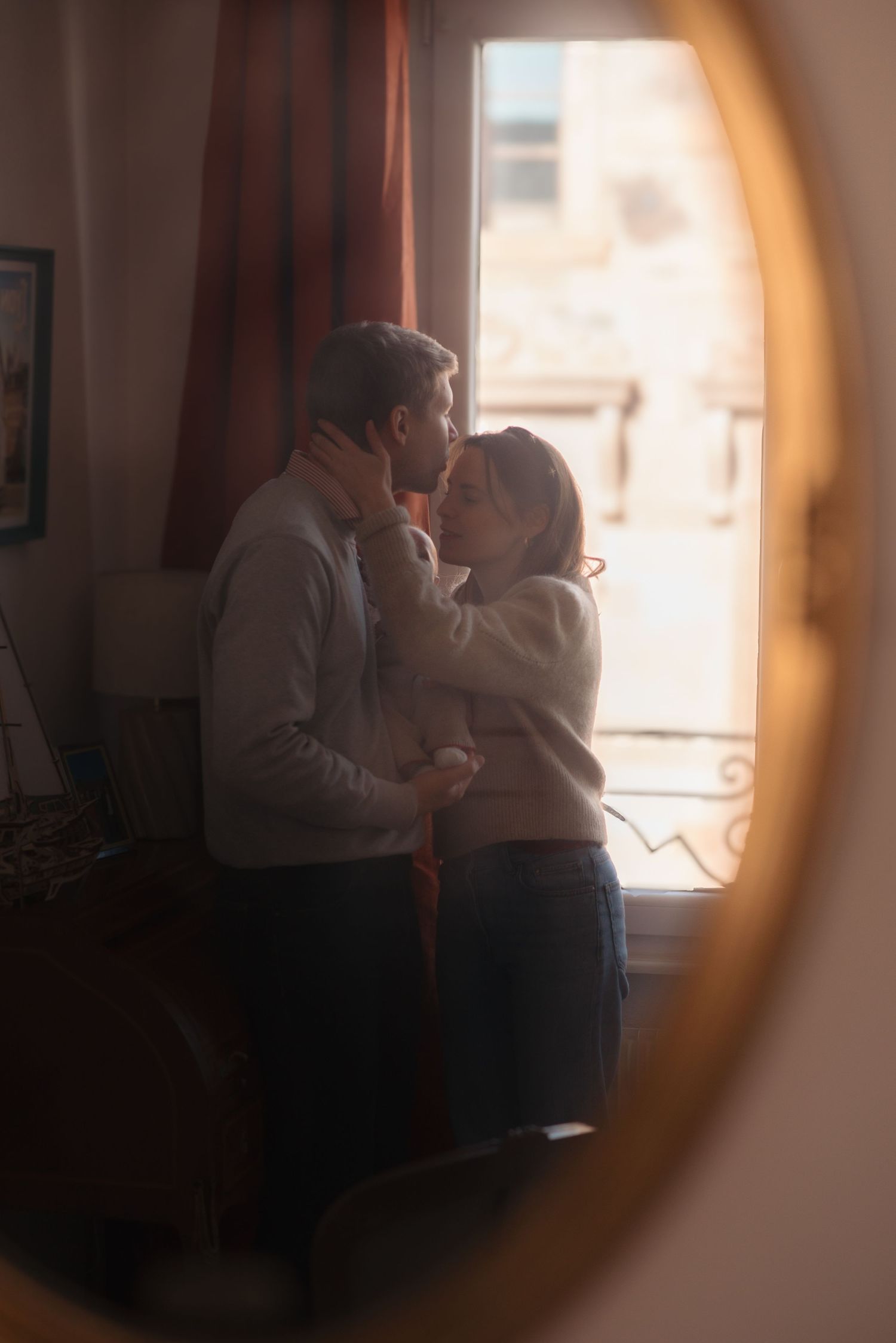 A romantic moment captured through a mirror reflection as a couple embraces near a window.