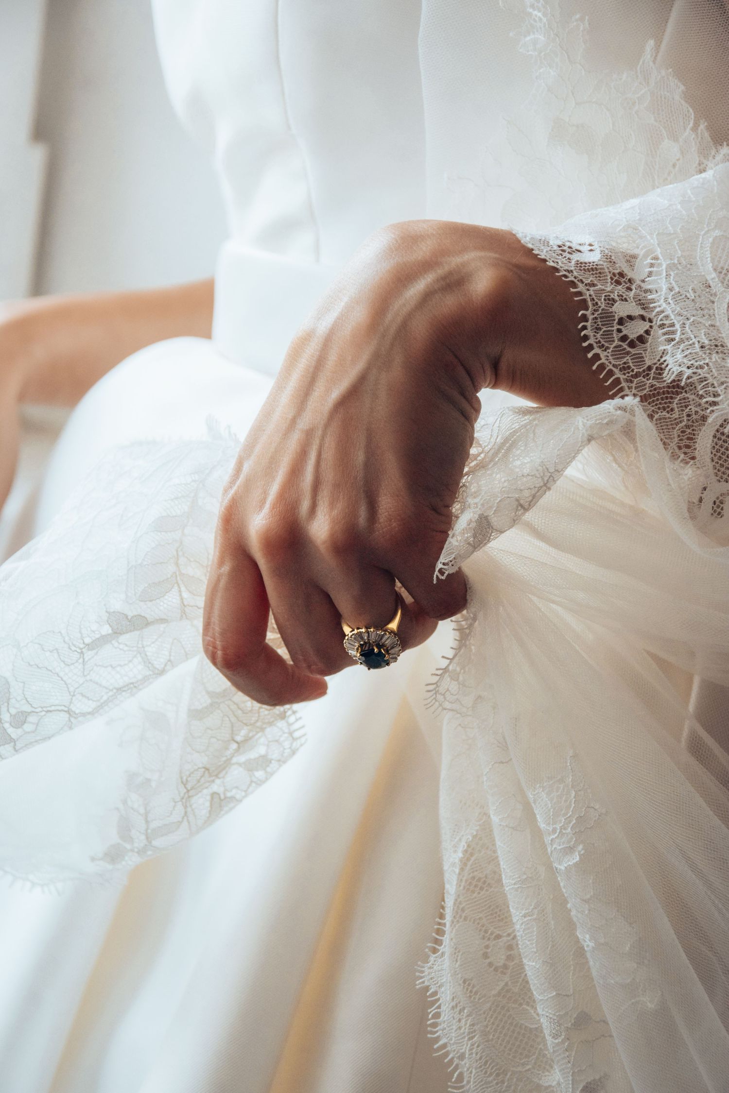 Close-up of bride's hand showing engagement ring against white lace wedding dress.