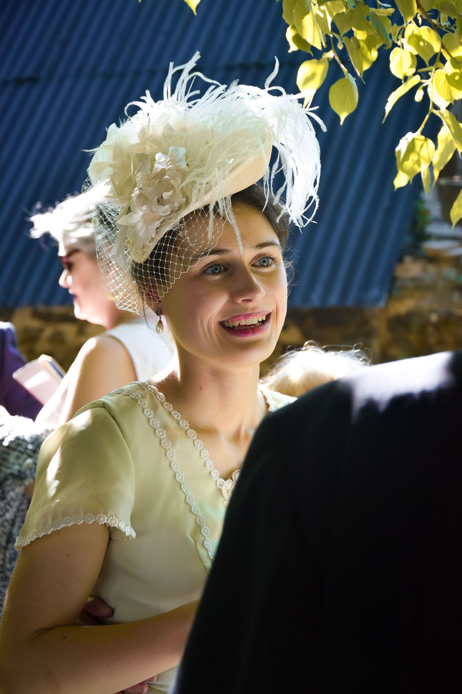 Guest in pale dress and elaborate white feathered fascinator at outdoor event.