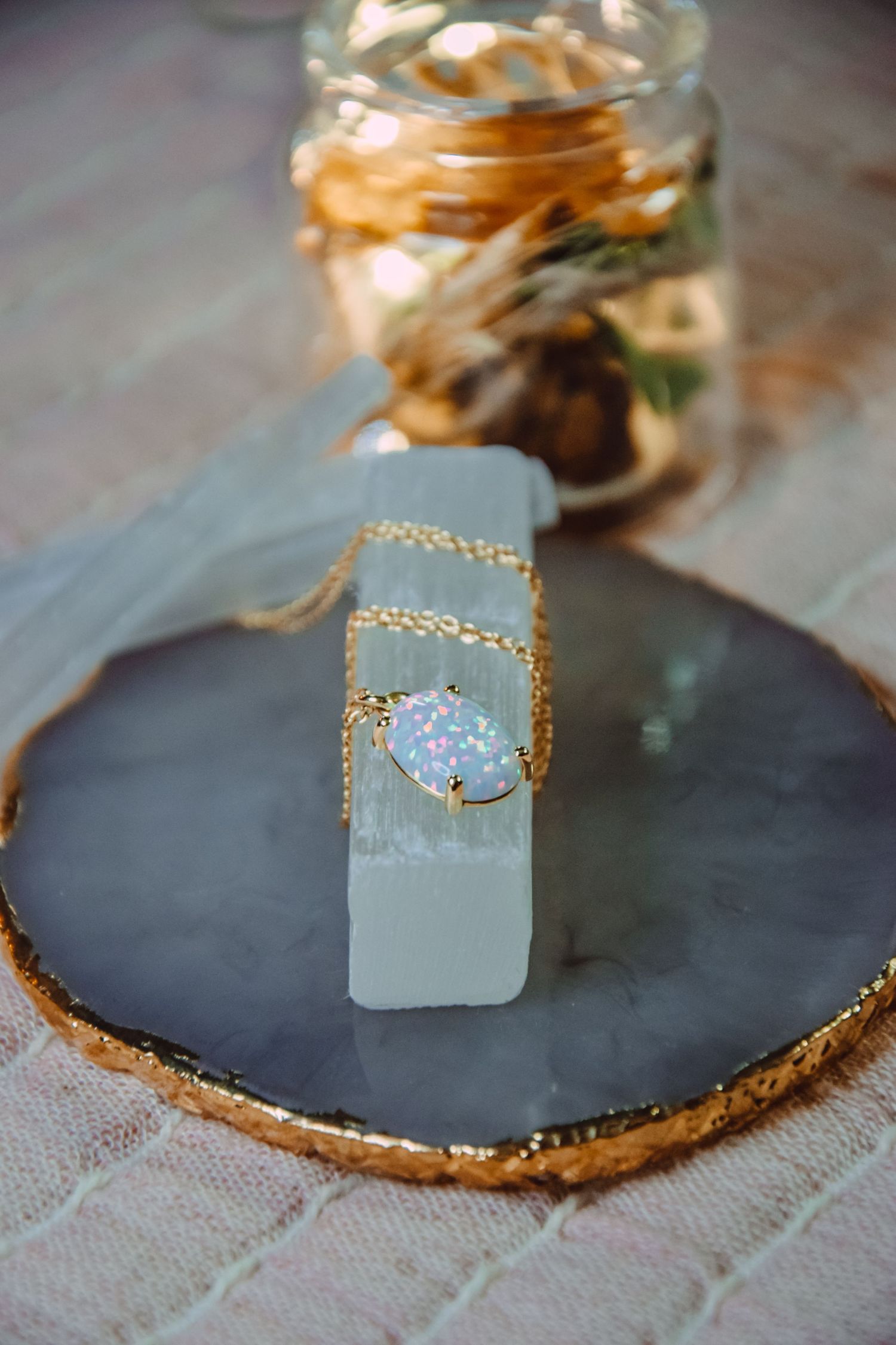 Crystal pendant necklace displayed on a black slate plate with gold trim and decorative jar in background.
