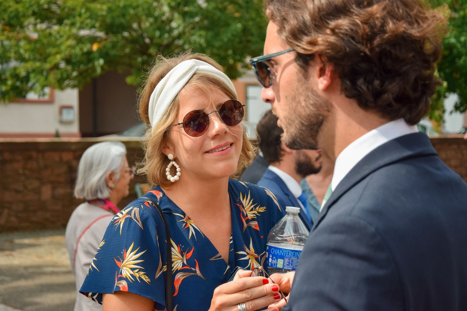 Wedding guests chatting at outdoor reception while holding drinks.