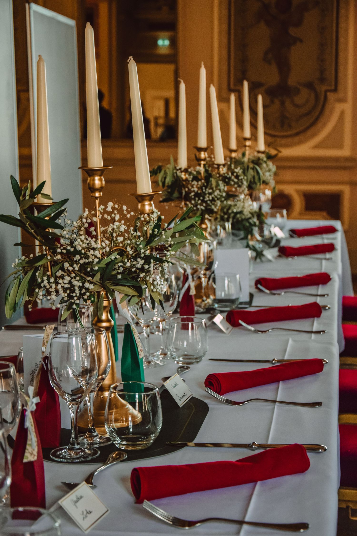 Elegant table setting with white candles, red napkins, and delicate floral arrangements for a formal dinner.