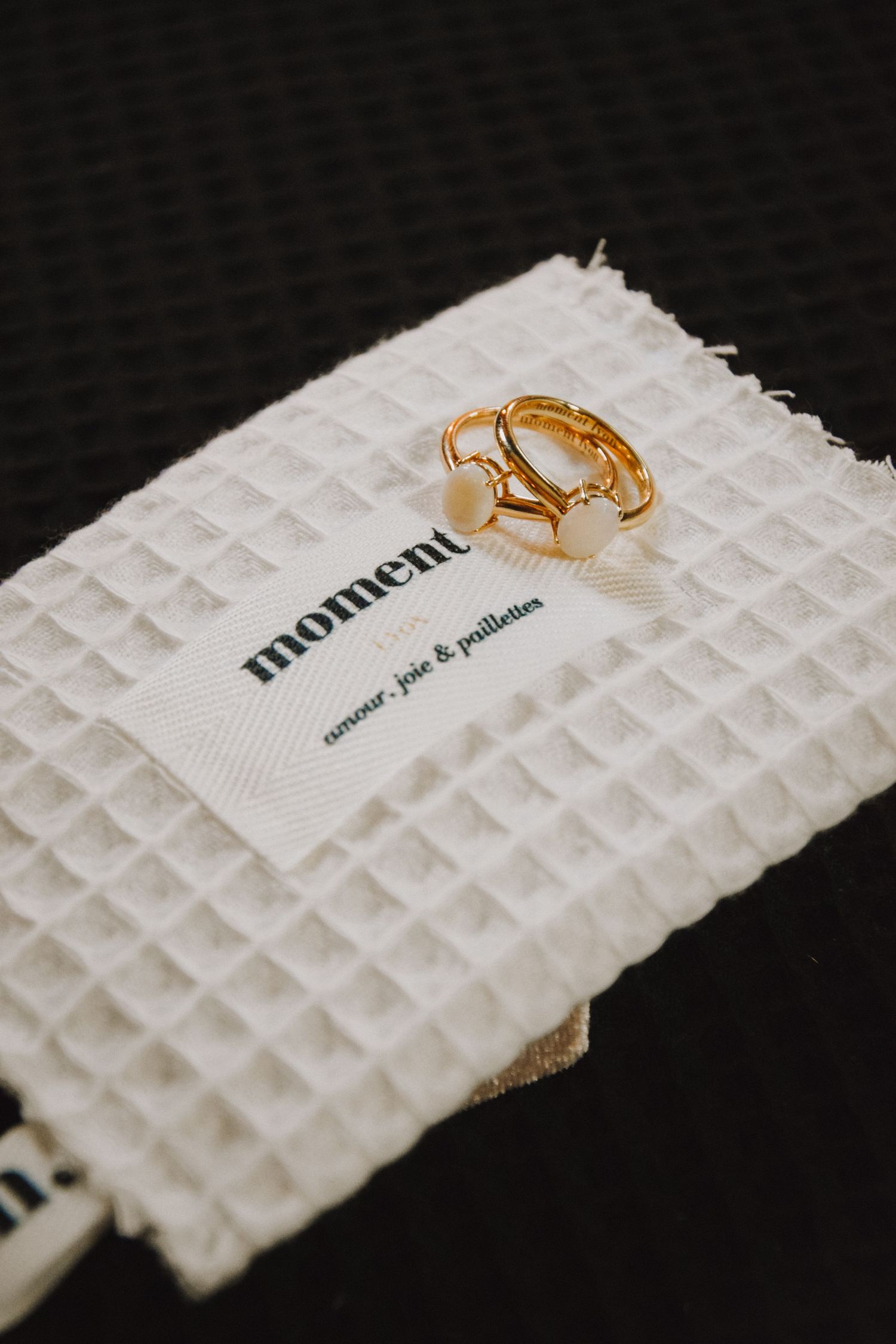 Gold geometric ring displayed on white textured fabric with 'moment' branding.