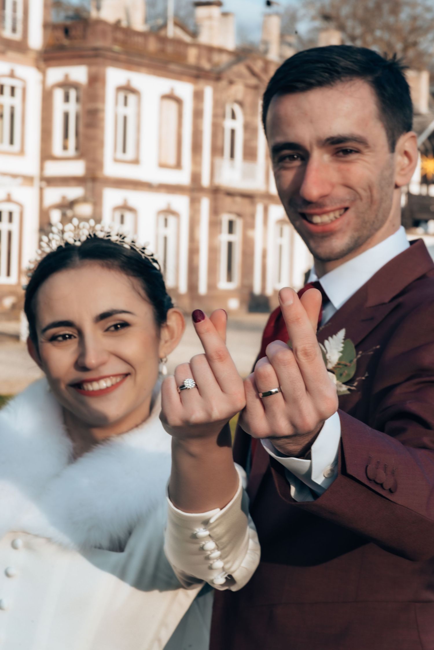 Newlyweds showing off their wedding rings together in front of a historic building.