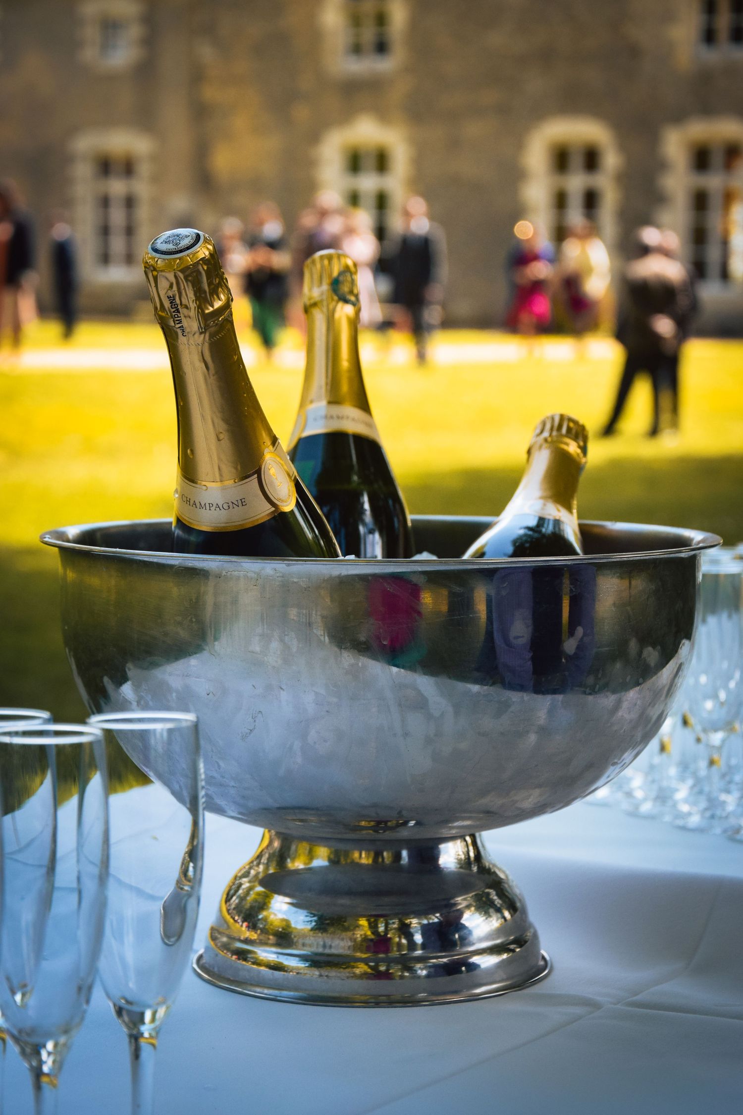 Champagne bottles chill in a silver ice bucket at an outdoor wedding reception.