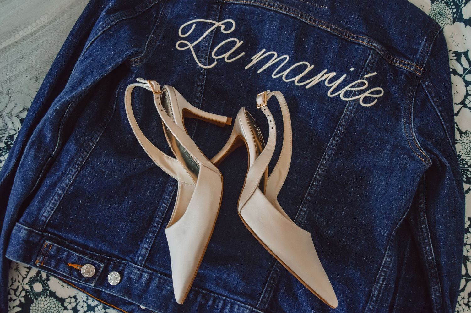 A pair of nude slingback heels placed on a blue denim jacket with 'La mariee' text embroidered on it.