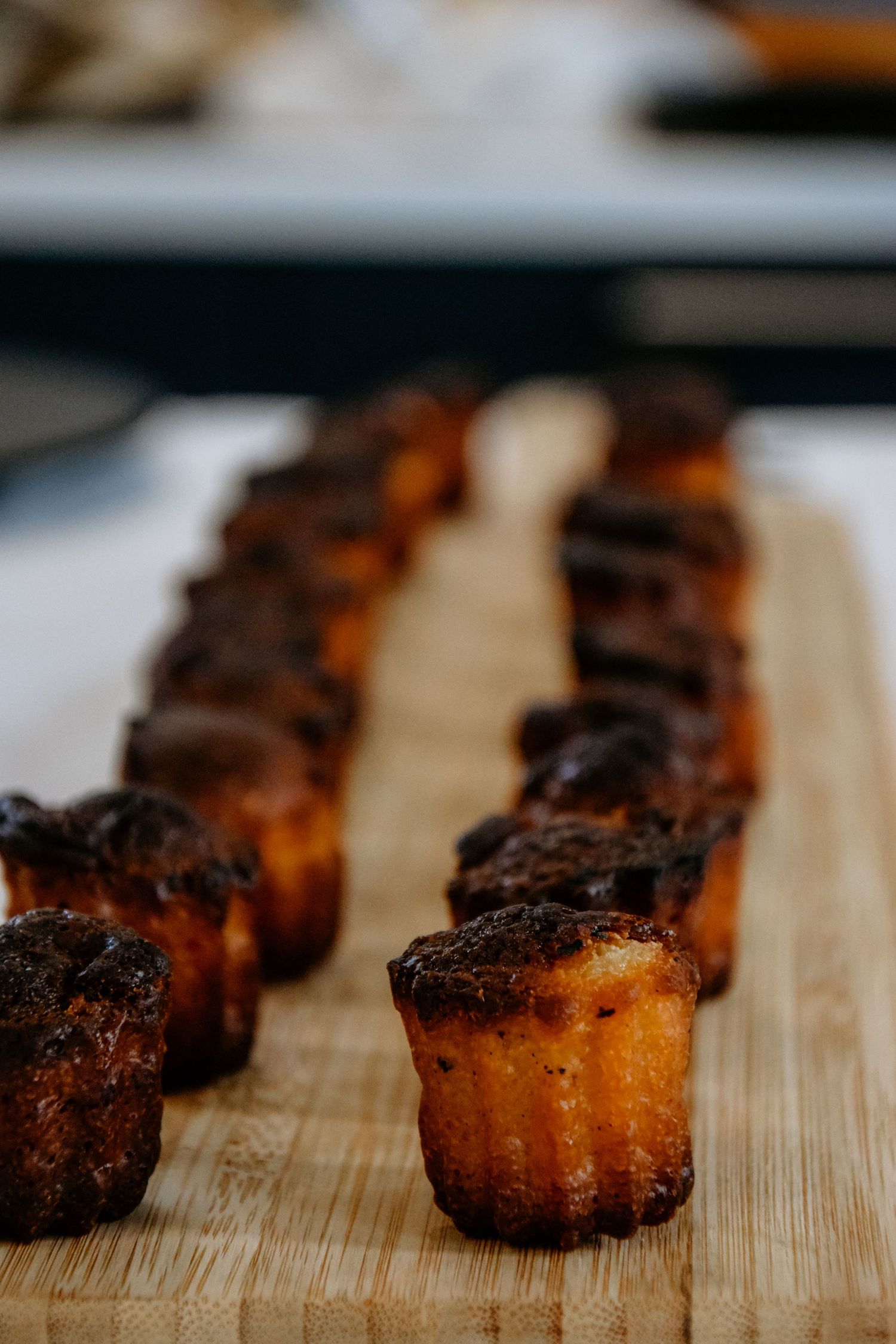 Row of caramelized caneles pastries lined up on a wooden cutting board.