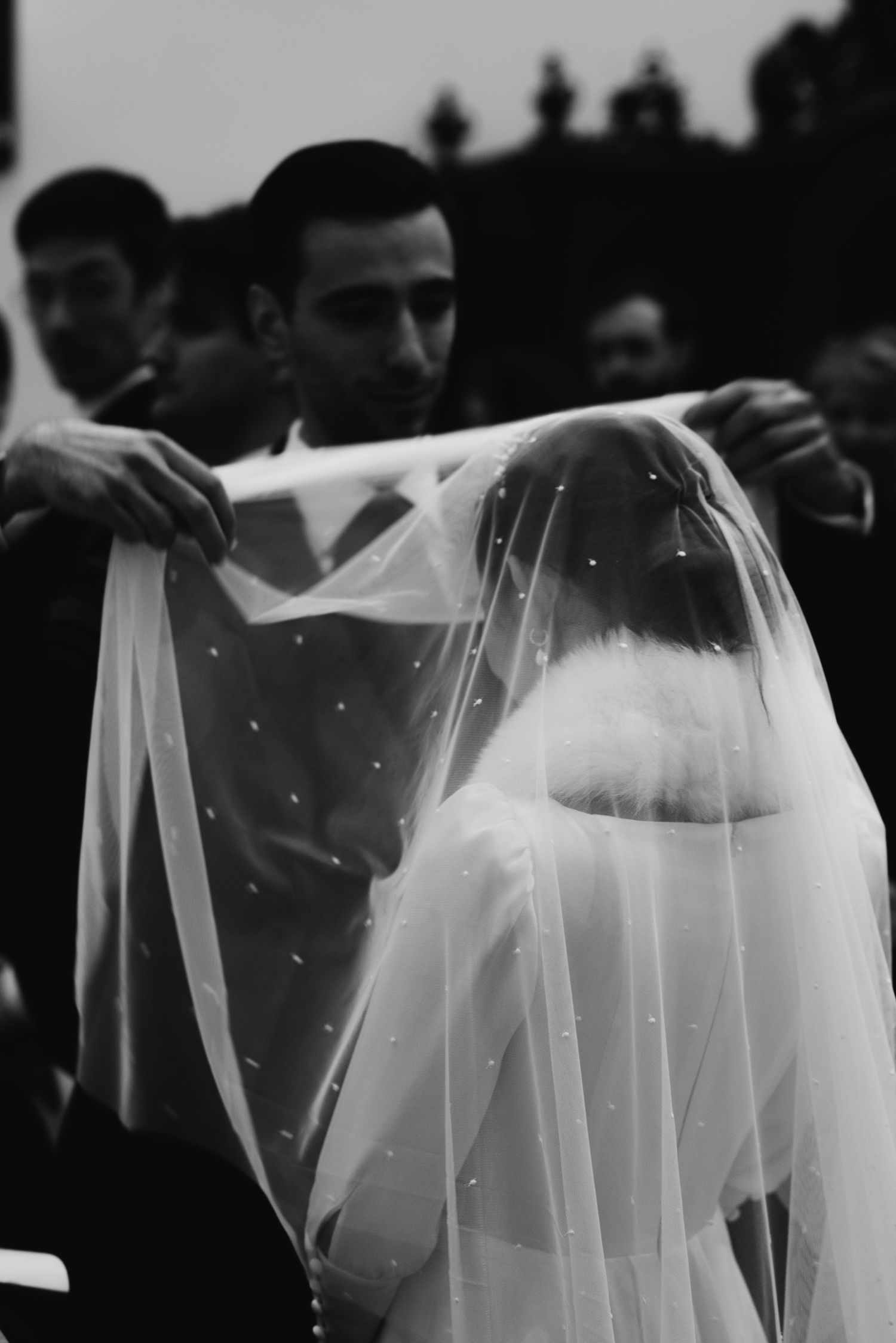 Black and white photo of a delicate bridal veil being adjusted during a wedding ceremony.