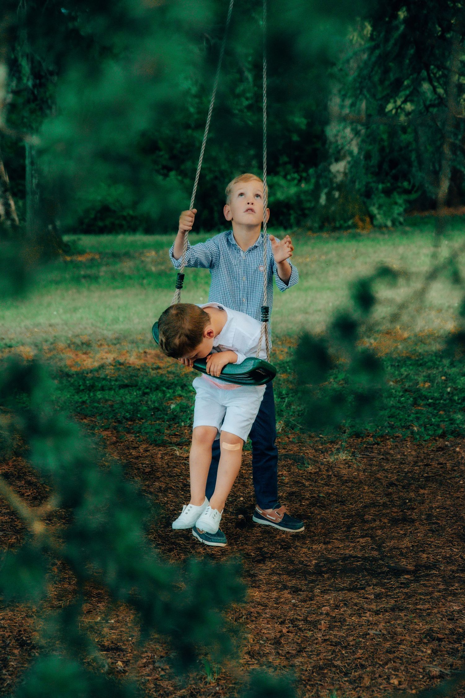 Two young children playing outside together with a rope swing in a lush green forest setting.