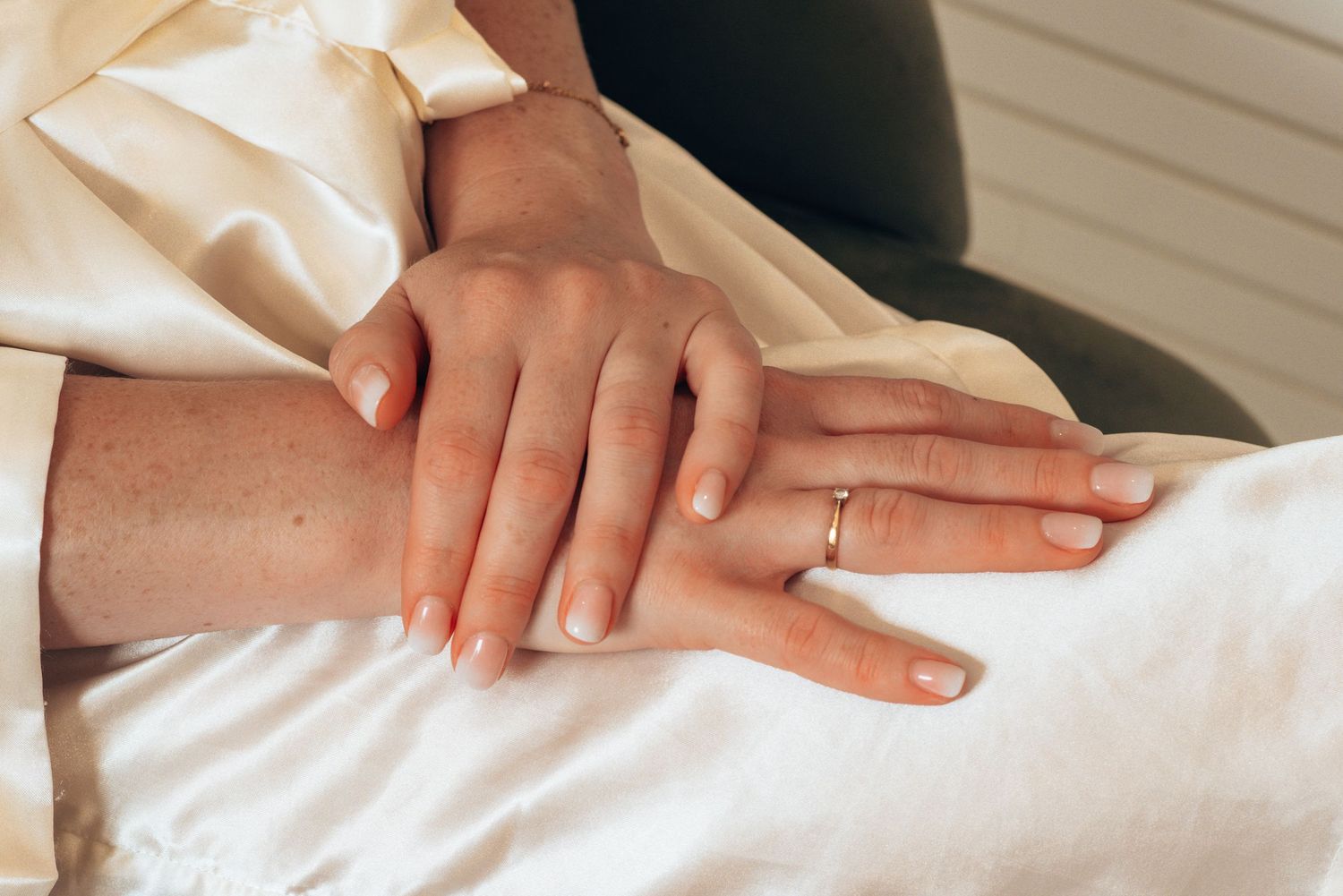 Two hands with simple wedding rings resting intimately together on white fabric.