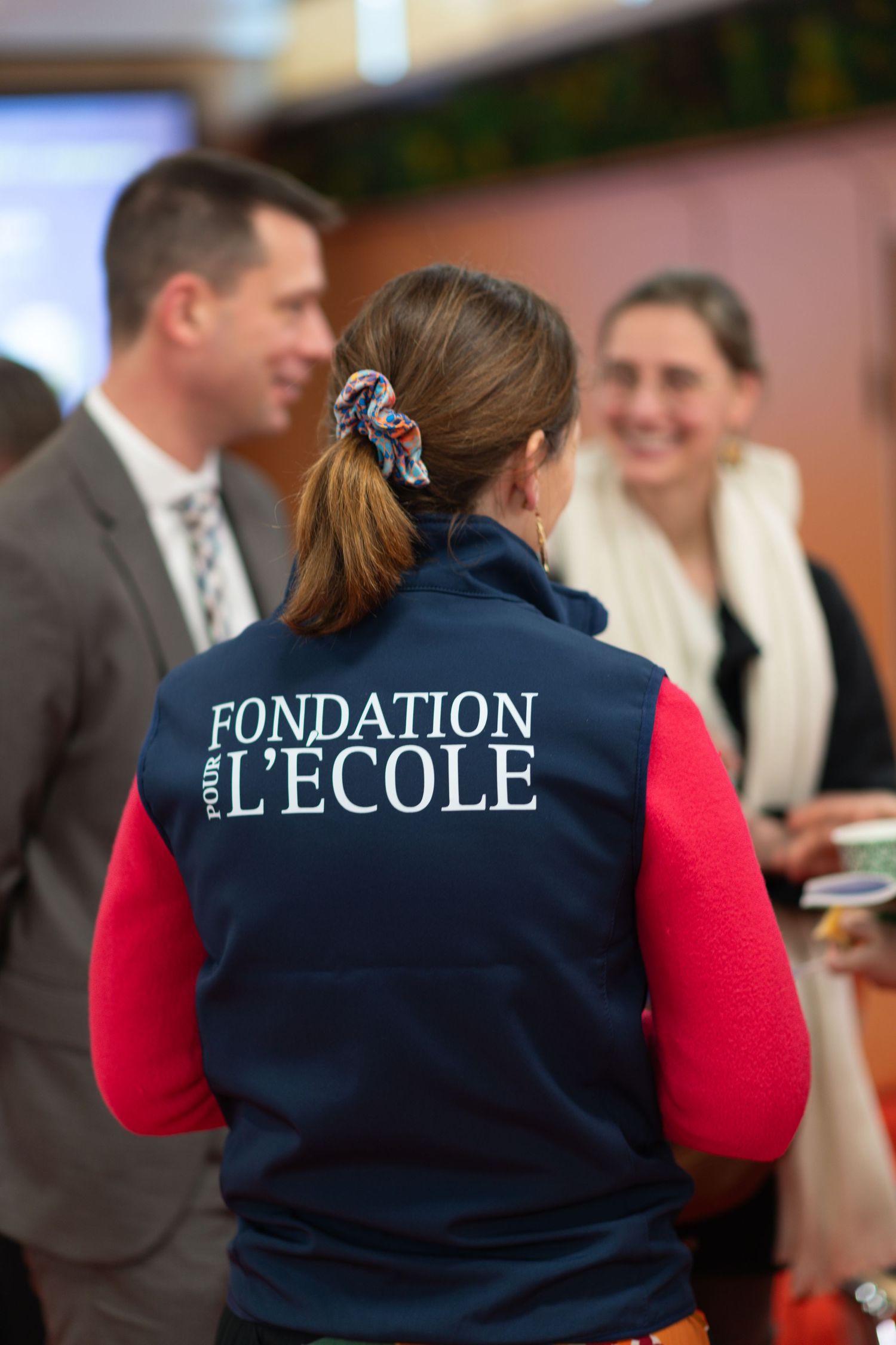 Person wearing navy and red Fondation L'Ecole vest at formal event.