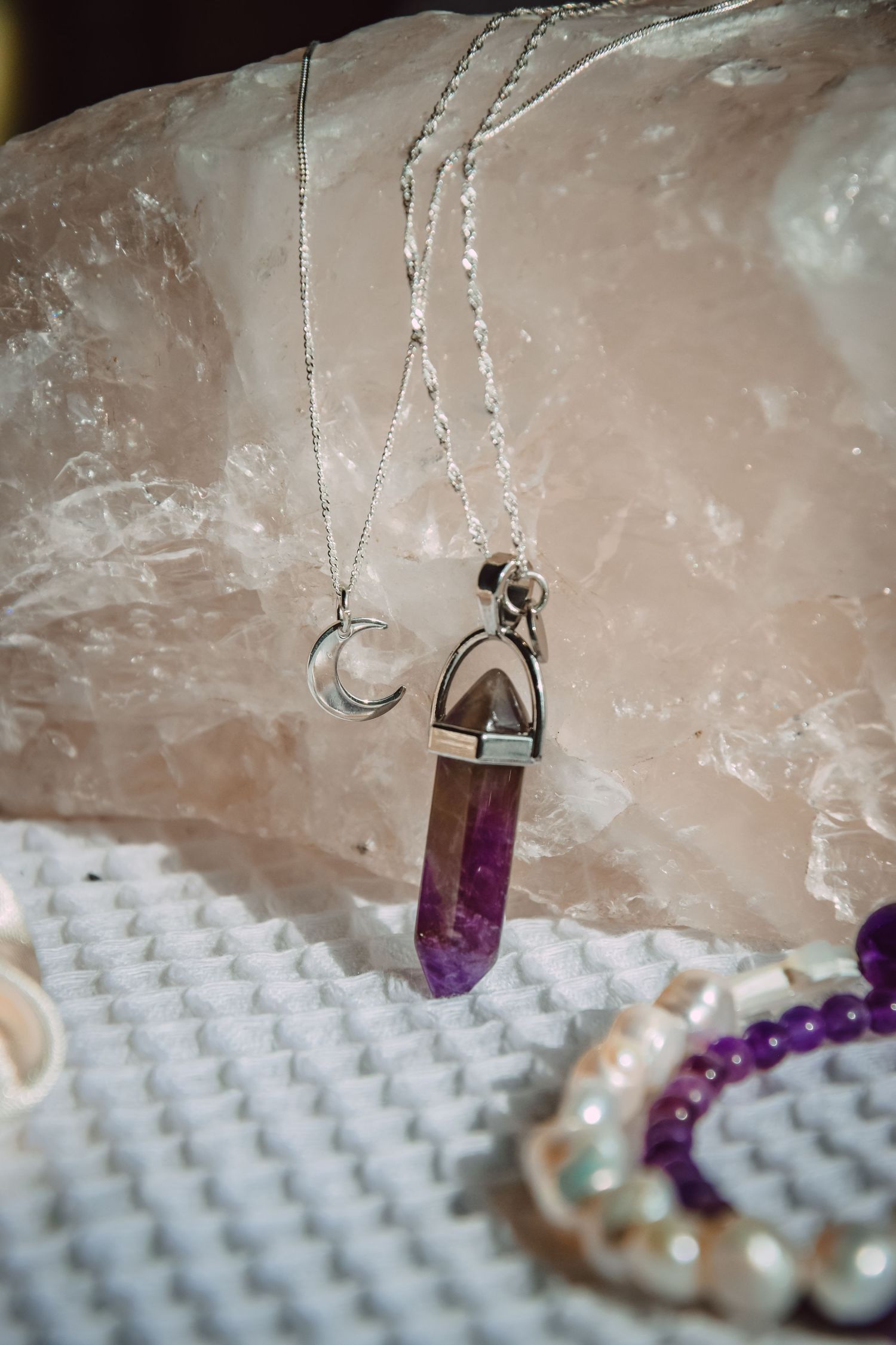 Crystal pendant necklaces with moon charm and purple gemstone displayed on white textured surface.