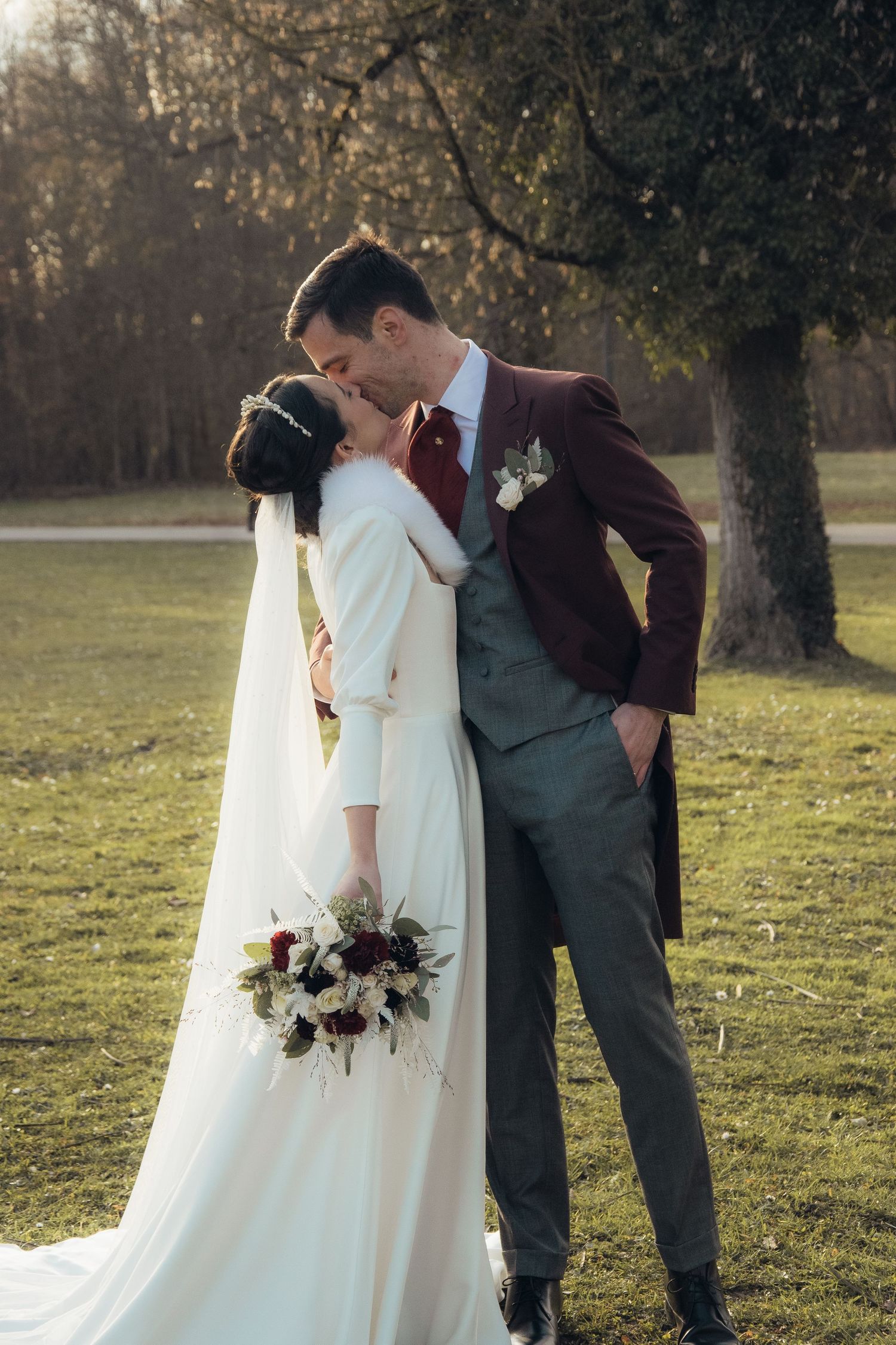 Romantic wedding couple sharing a kiss in an outdoor setting with autumn trees in the background.