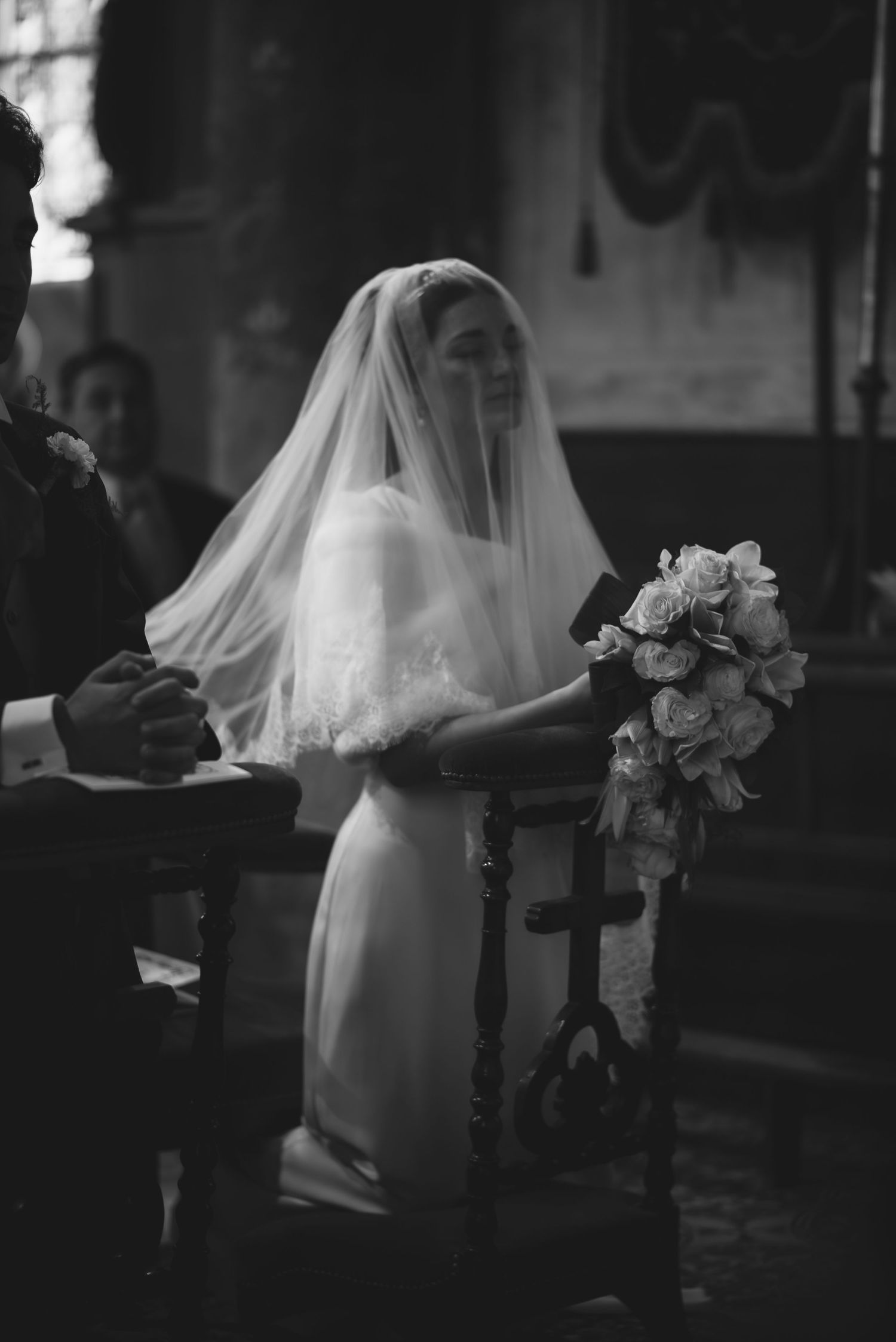 Classic black and white image of bride in wedding gown holding bouquet during ceremony.