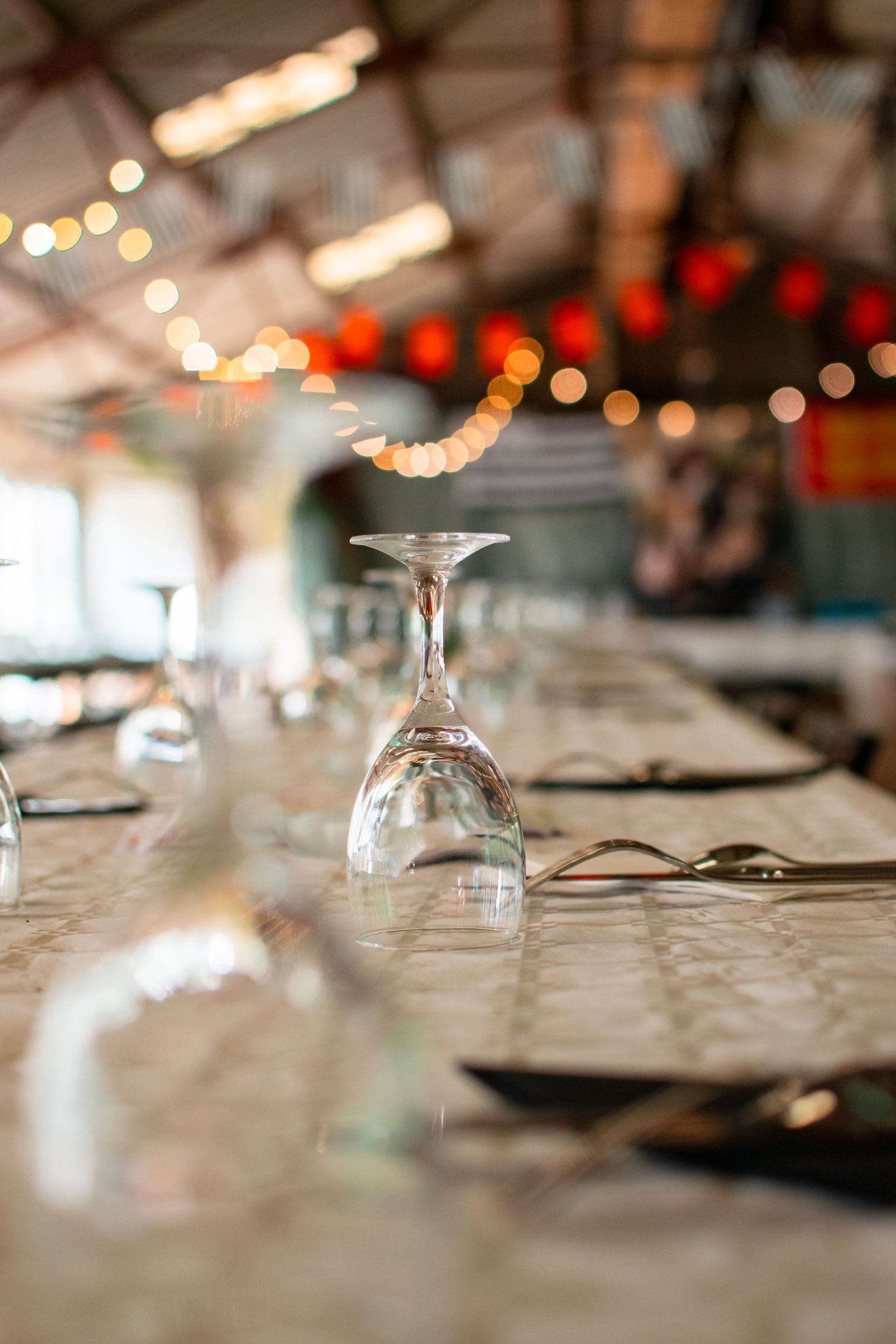 Upturned wine glasses on set table with string lights in background creating bokeh effect.