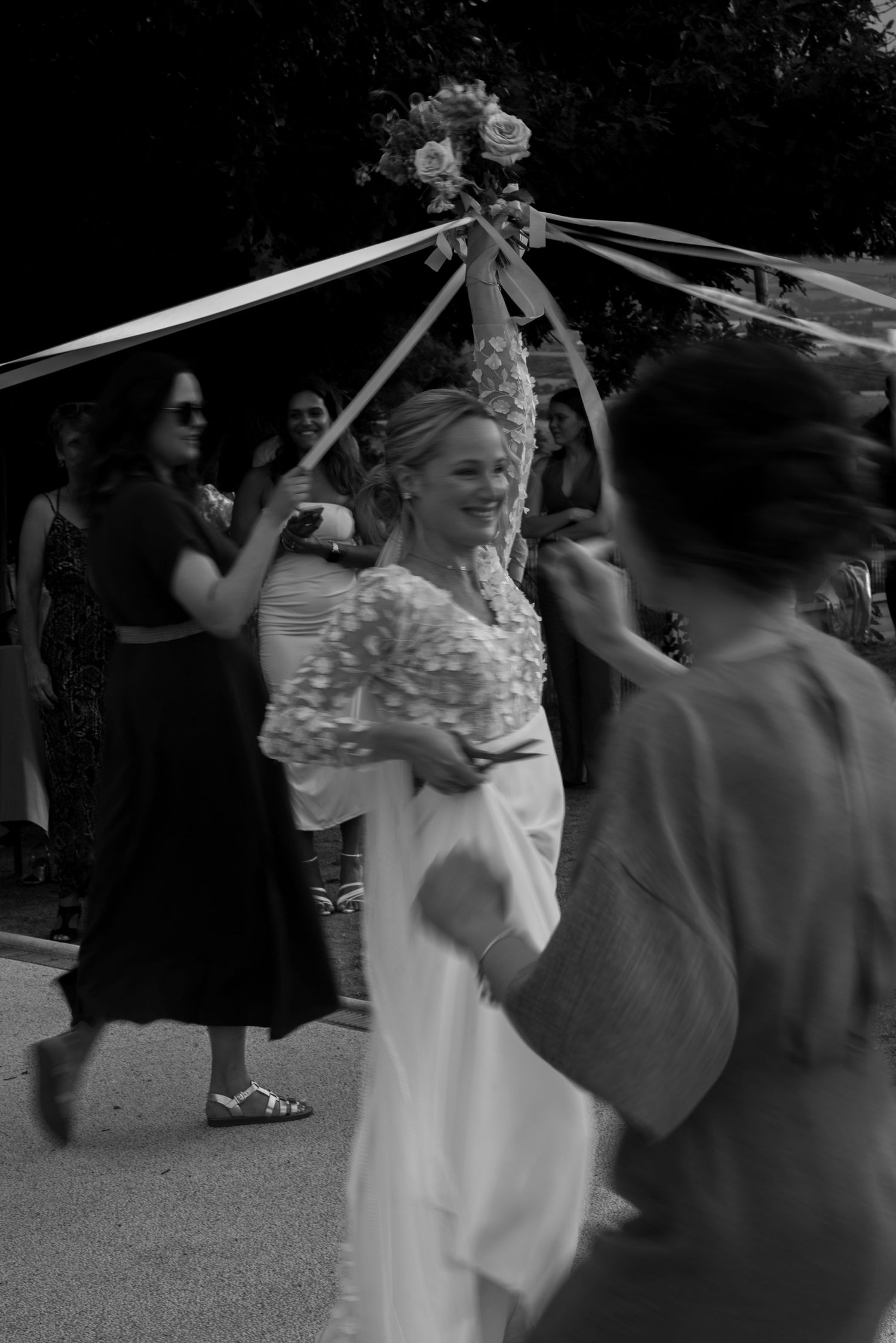 People participate in a traditional wedding ceremony ritual outdoors with decorative ribbons in black and white.