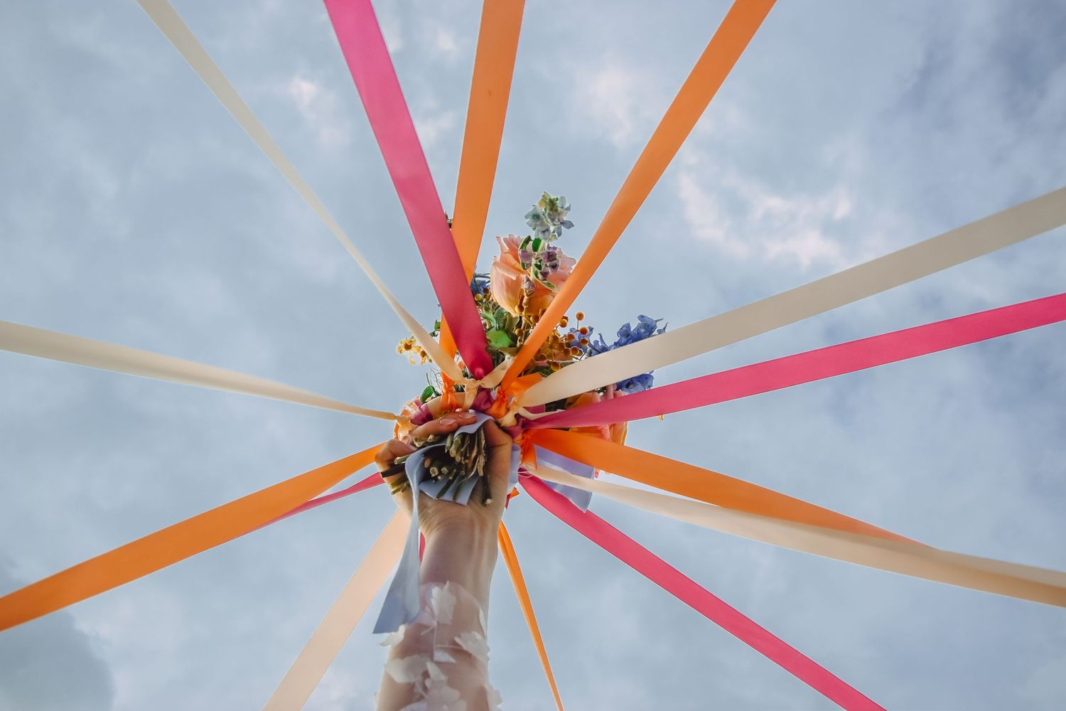 Colorful streamers and orange flowers burst outward against a cloudy blue sky in a decorative maypole design.