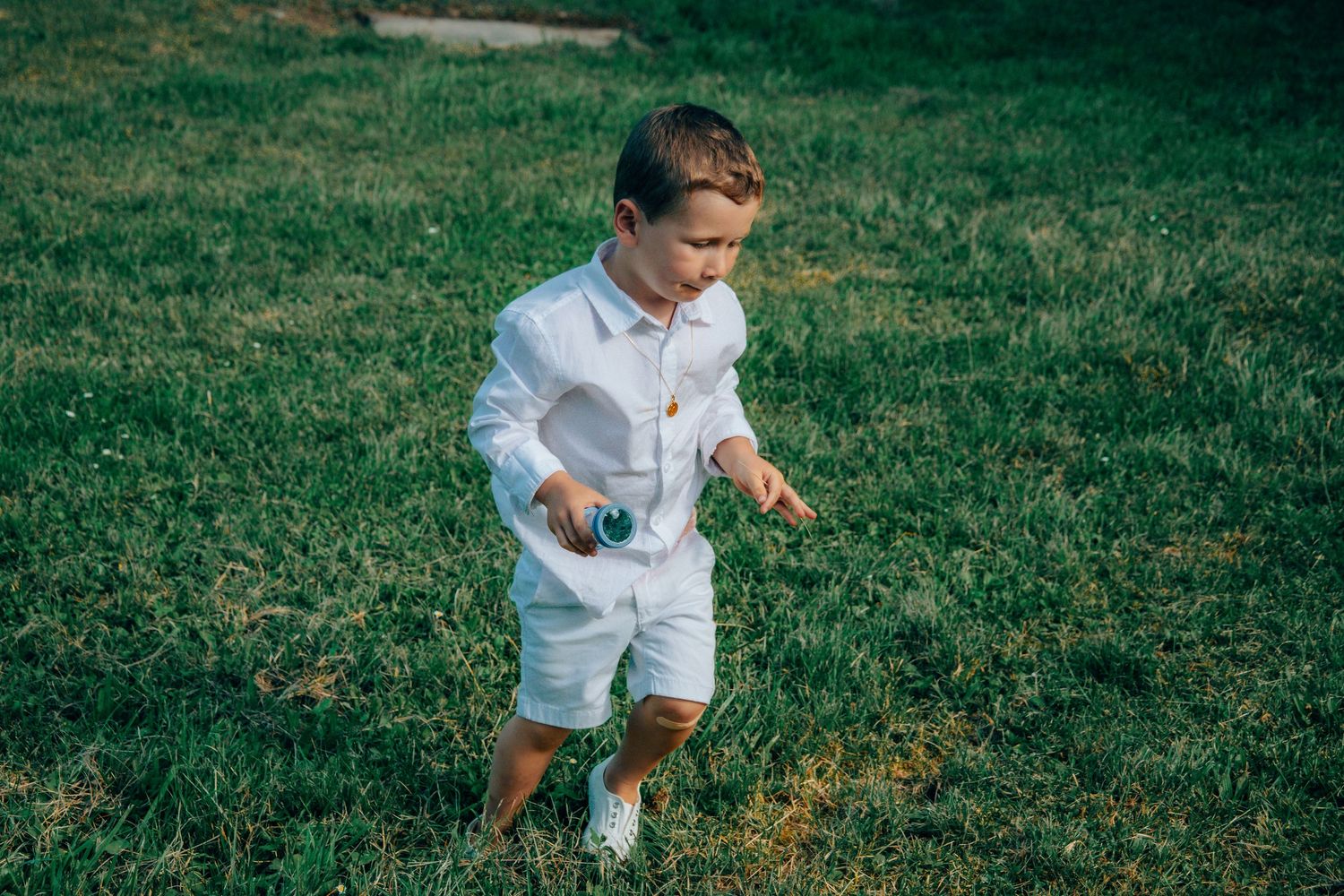 A young child in white clothing runs playfully across a green lawn on a sunny day.