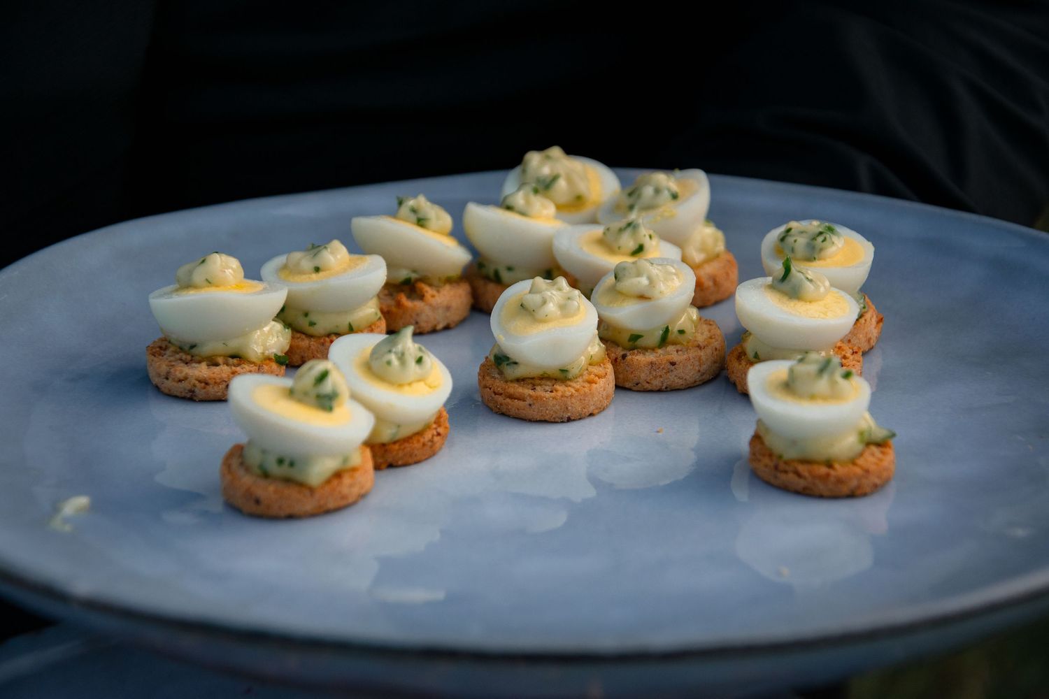 Close up shots of boiled egg and cracker canapes being arranged on gray plates for serving.