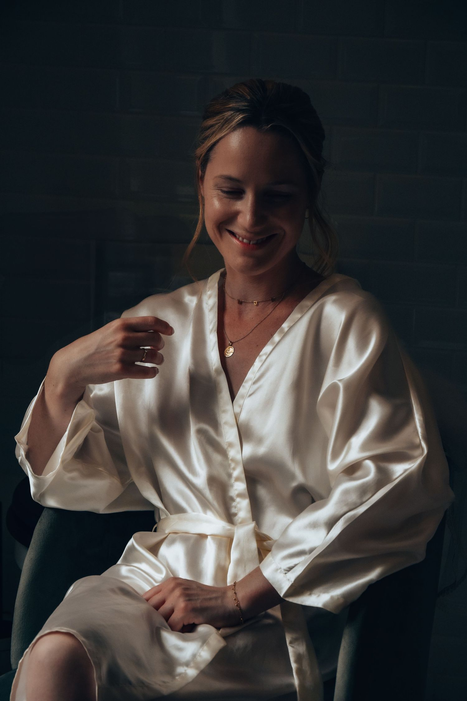 Person in white silk robe smiles during wedding morning preparations.