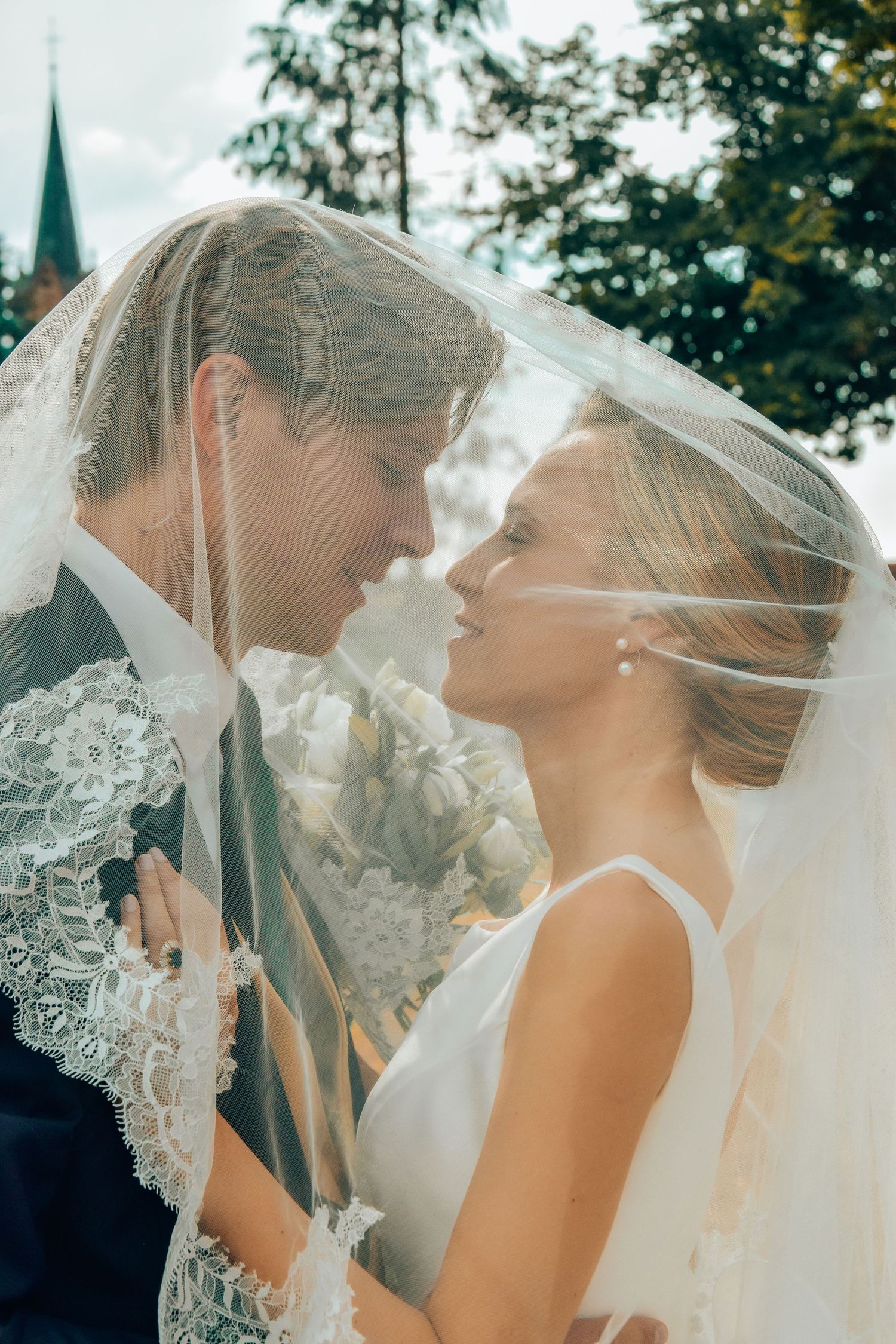 Romantic moment between couple under delicate lace veil outdoors.