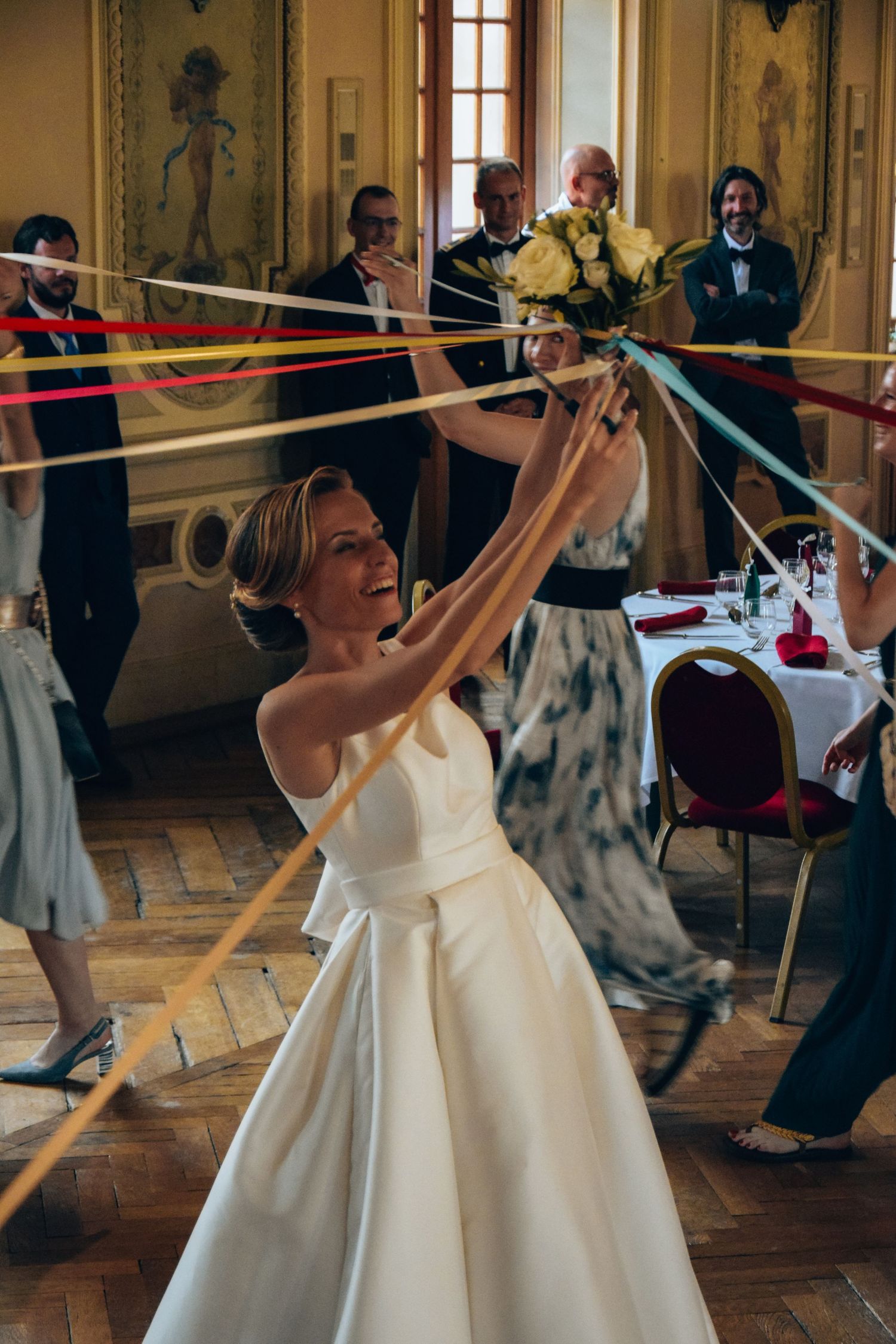A joyful wedding reception game with colorful ribbons in an ornate ballroom setting.