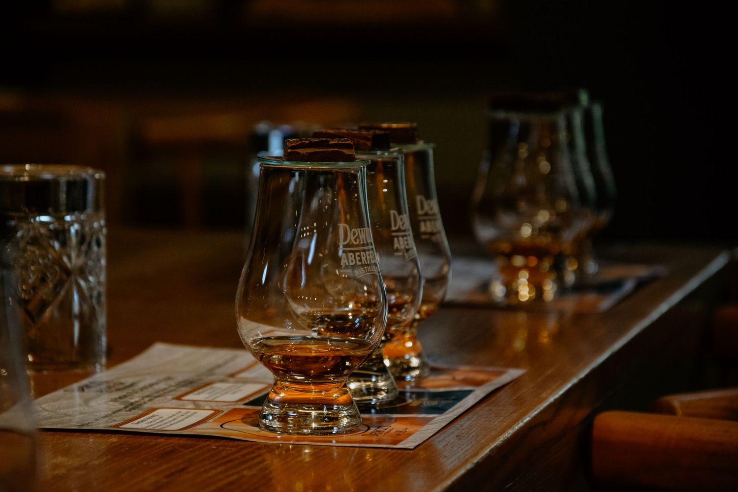 Several whiskey tasting glasses lined up on a wooden table in dim lighting.