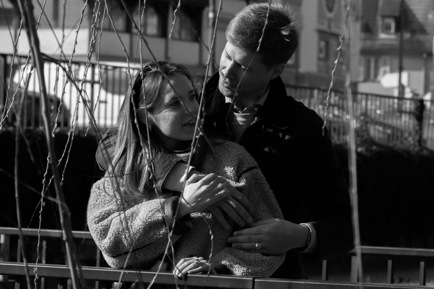 Black and white photo of two people sharing a tender moment outdoors by a railing.