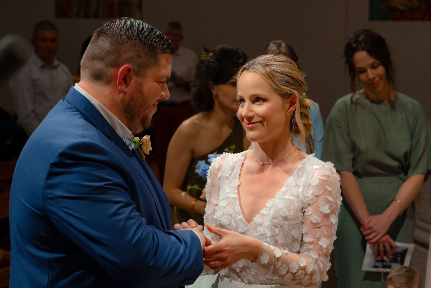 A couple stands close together during a wedding ceremony as they exchange rings in a warmly lit indoor setting.