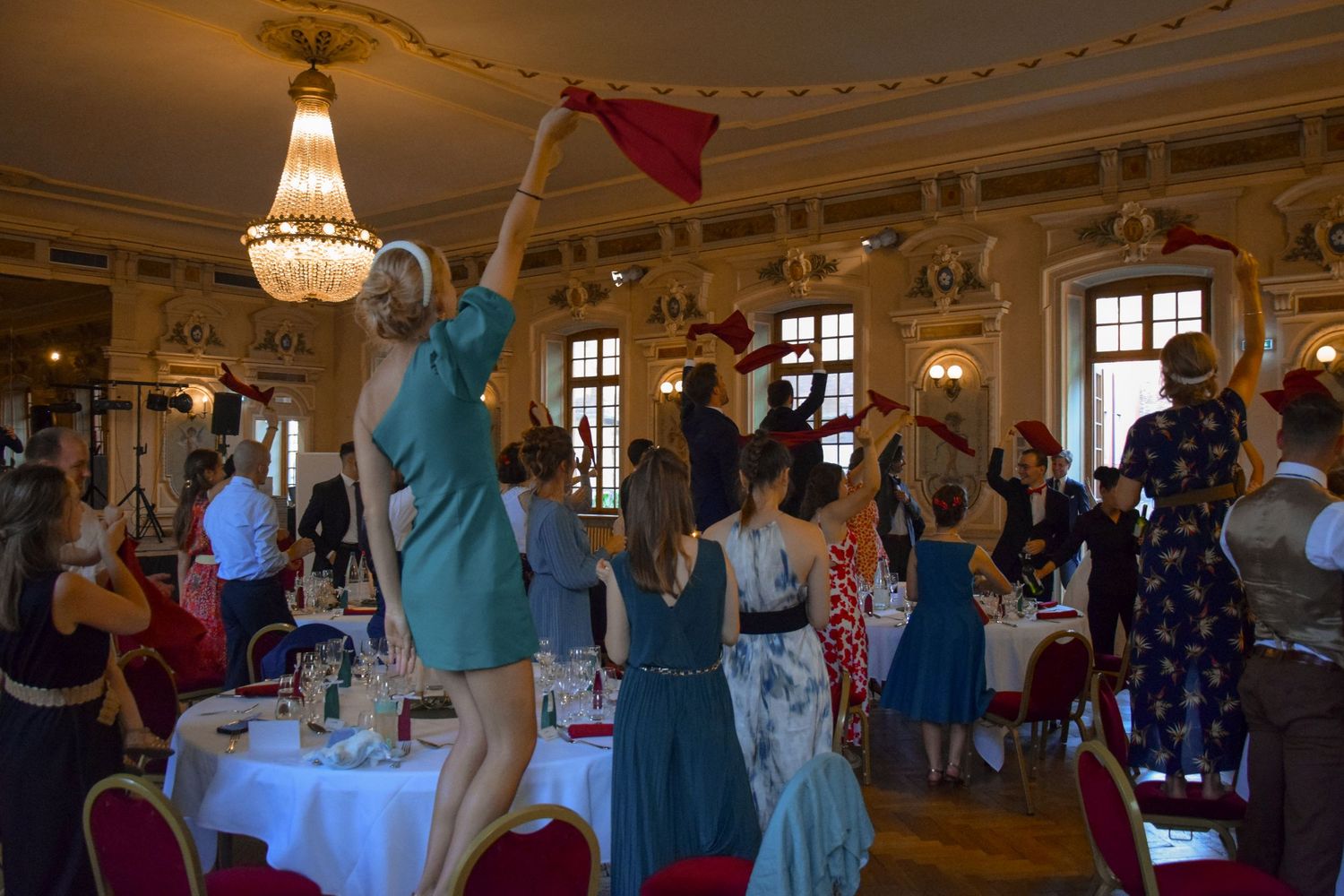 Wedding guests dancing and celebrating in an elegant ballroom with crystal chandeliers.