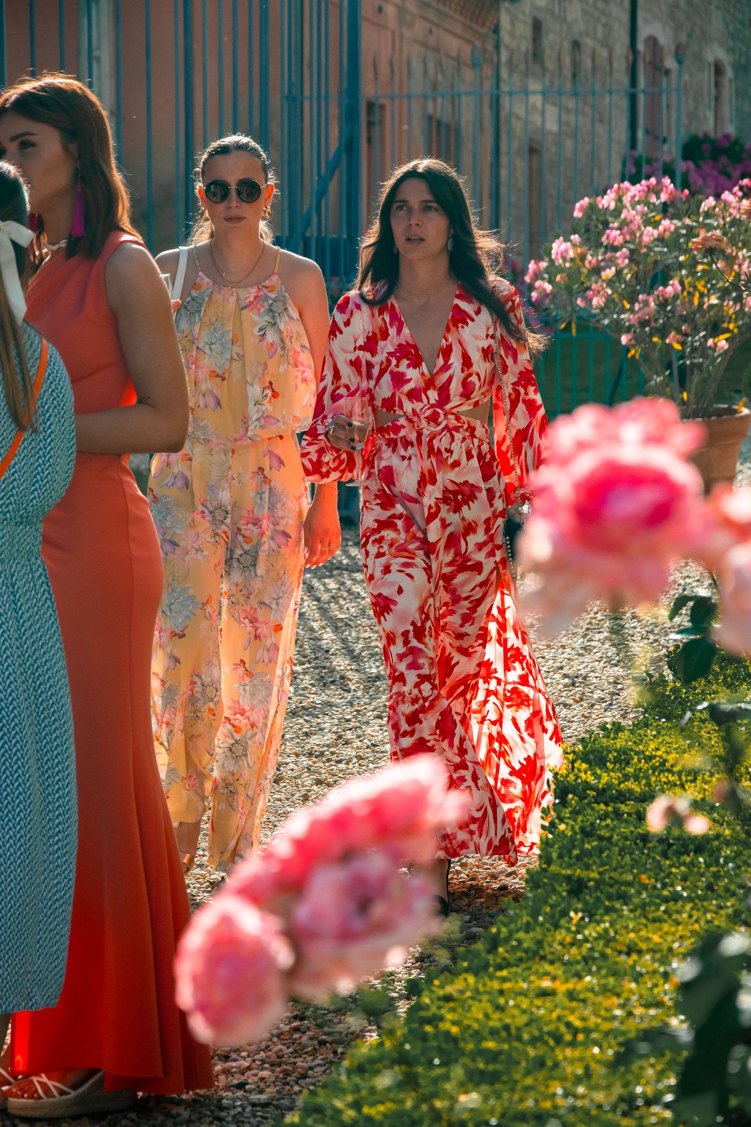 Women in colorful summer dresses walking through a garden path with blooming roses.