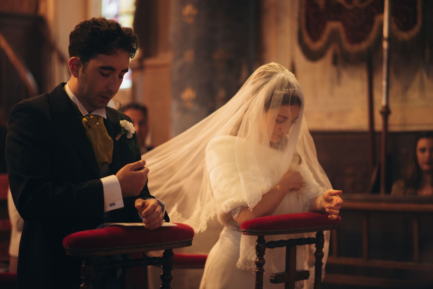 Couple at wedding ceremony with bride in white veil reading from red book.