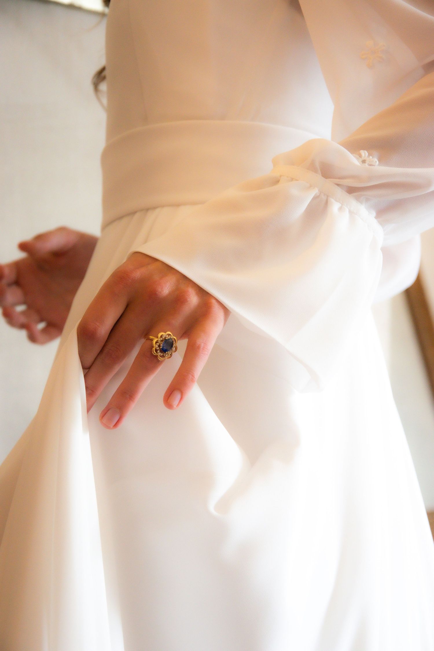 Close-up of an ornate vintage ring on hand against flowing white wedding dress fabric.