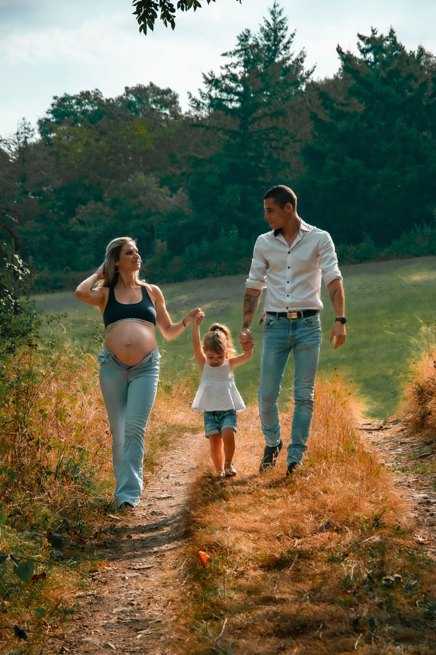 Family taking a peaceful walk together on a dirt trail through golden fields and evergreen forest on a warm summer evening.
