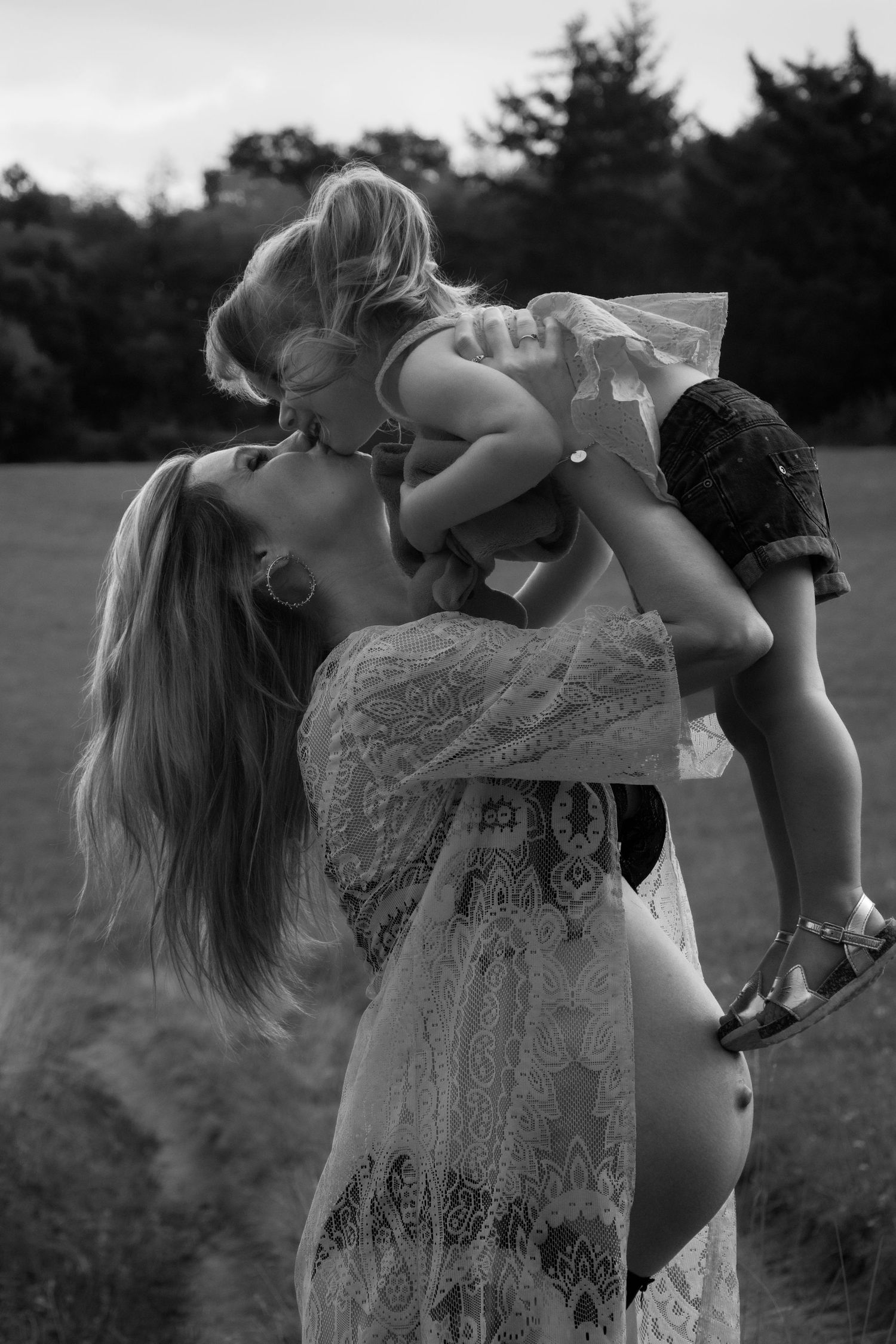 An artistic black and white maternity photo of a tender mother-daughter moment outdoors.