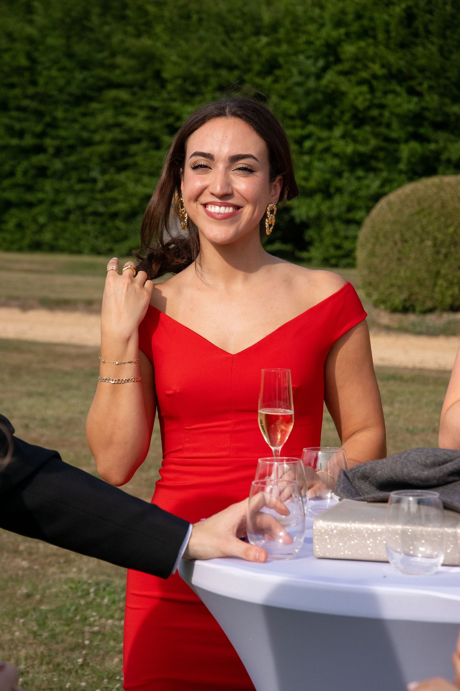 Woman in red dress smiling with champagne glass at outdoor celebration event.