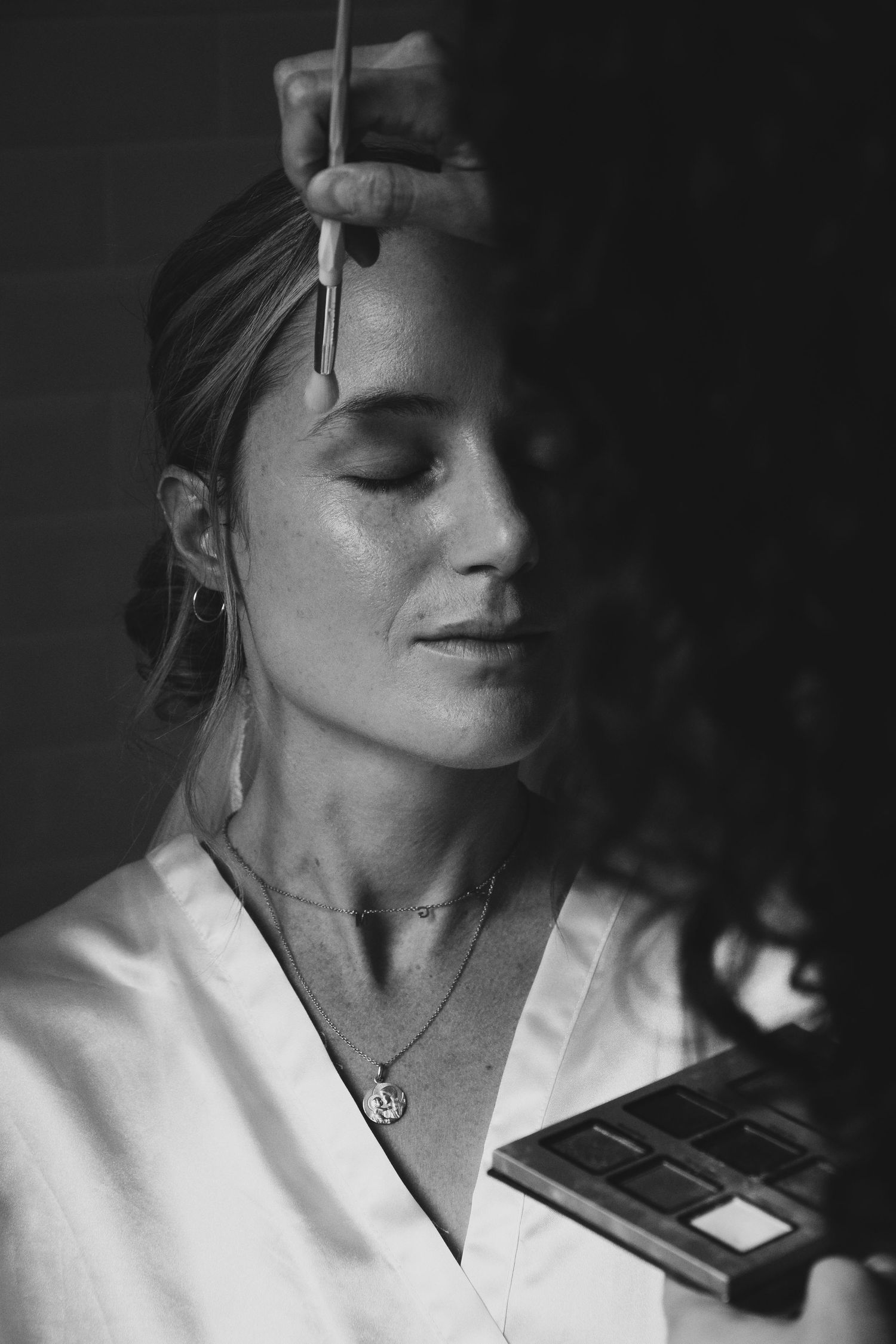 Black and white portrait shot featuring someone in a white blouse with eyes closed, jewelry, and hair pulled back.