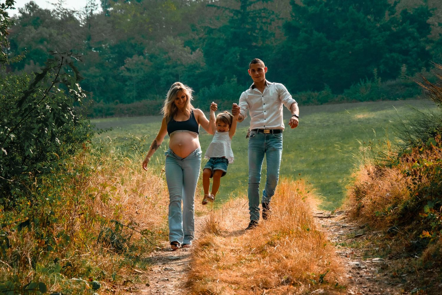 Family walking together on a sunlit dirt path through a scenic meadow.