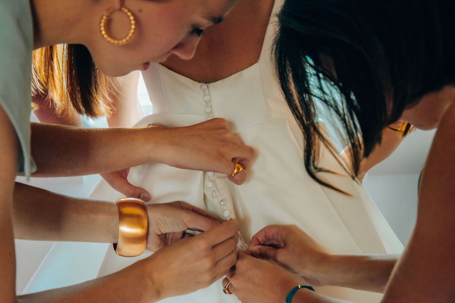 Hands working together to fix details on a white wedding dress.