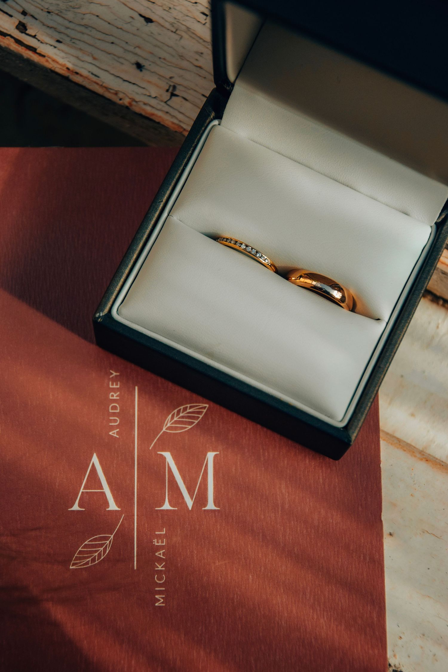 Gold wedding band in navy box with elegant AM monogram design on terracotta paper.