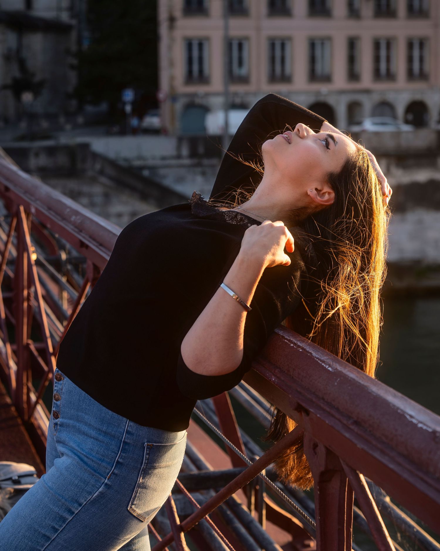 Woman gazes upward while leaning against a metal railing at sunset, creating a warm silhouette against the evening sky.