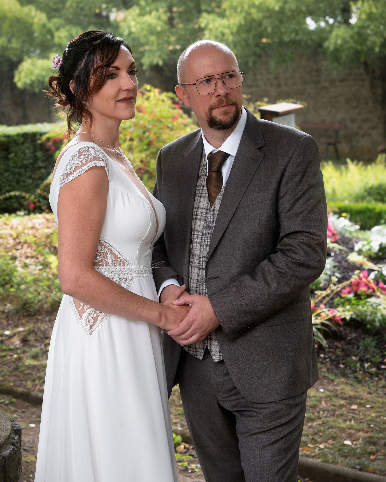 A couple shares tender moments outdoors in a garden while wearing formal wedding attire on their special day.