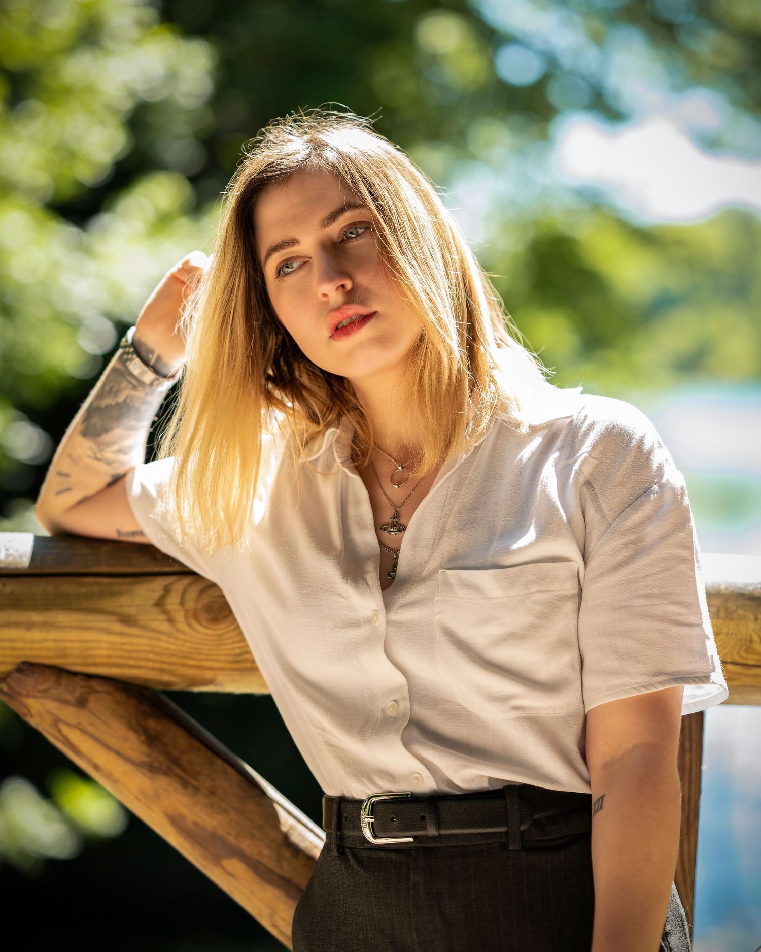 Woman in white shirt rests against wooden surface in soft natural lighting with blurred greenery background.