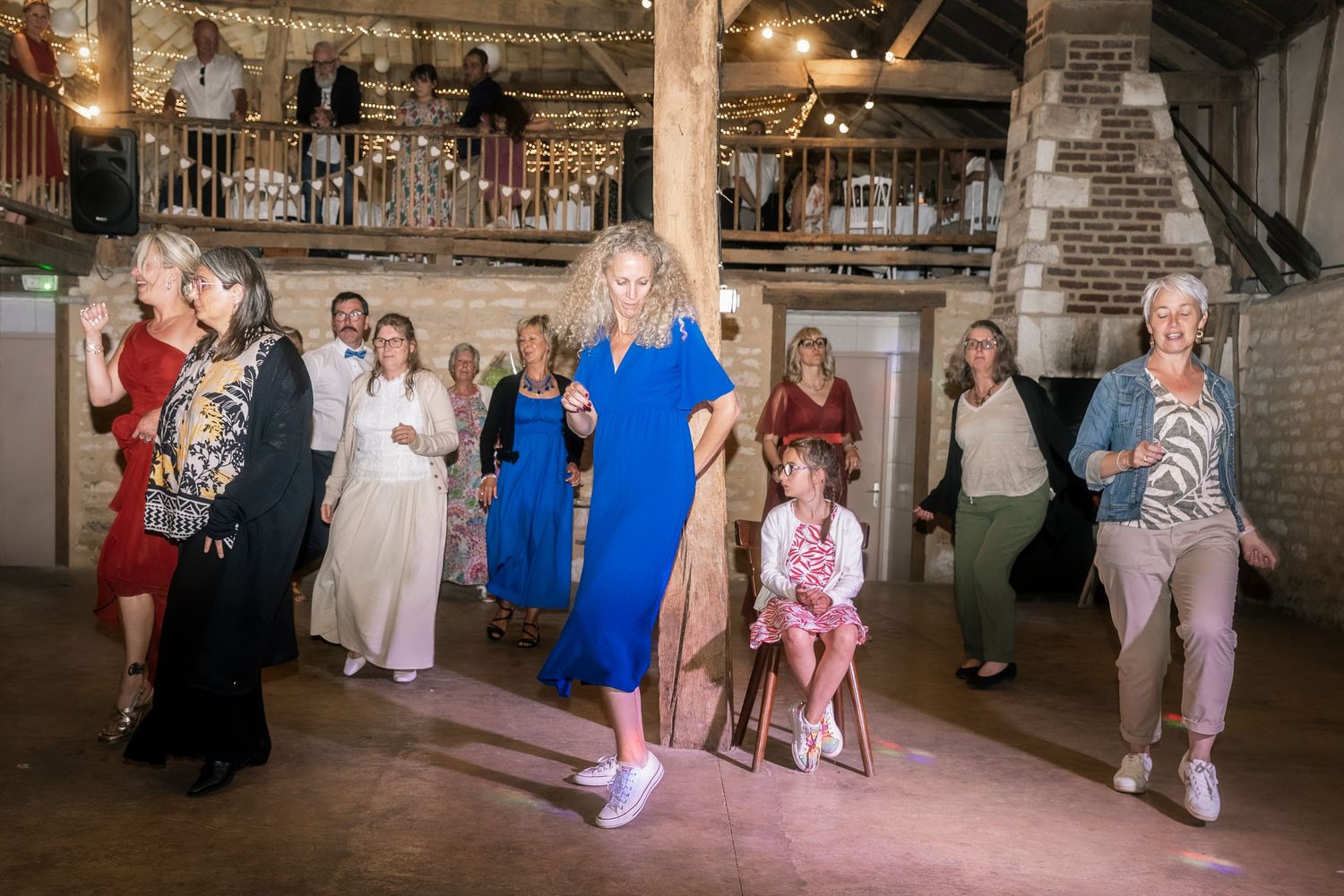A group of people dancing together at a rustic venue with exposed brick walls and wooden beams.